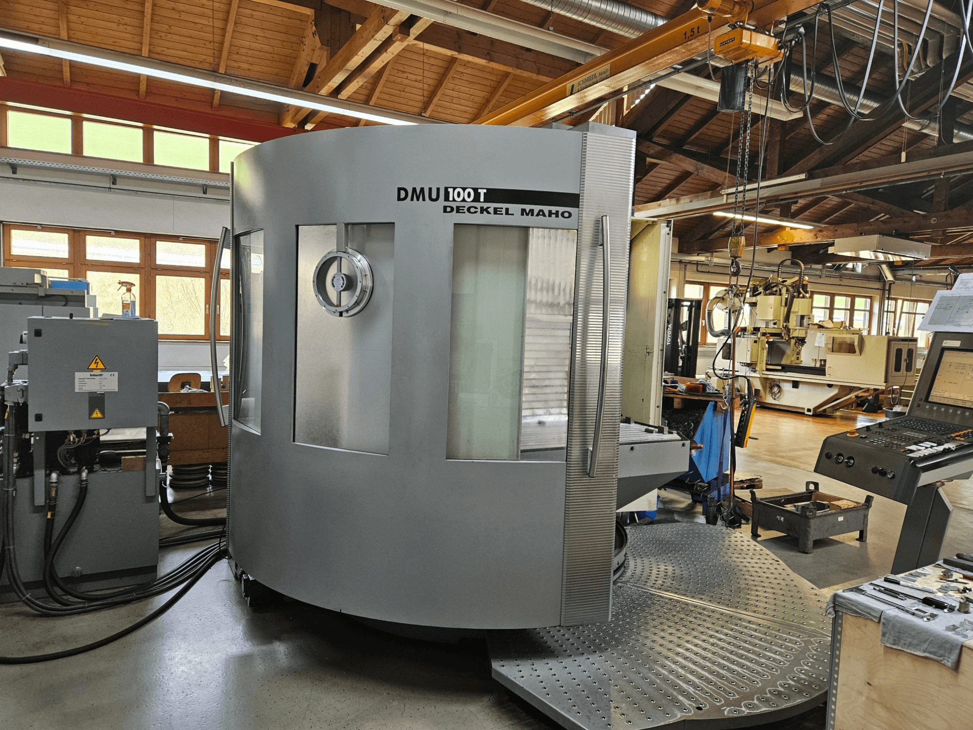 DMU 100 T Deckel Maho CNC-maskin sedd framifrån, med stor cirkulär bas, kontrollpanel och glashölje.
