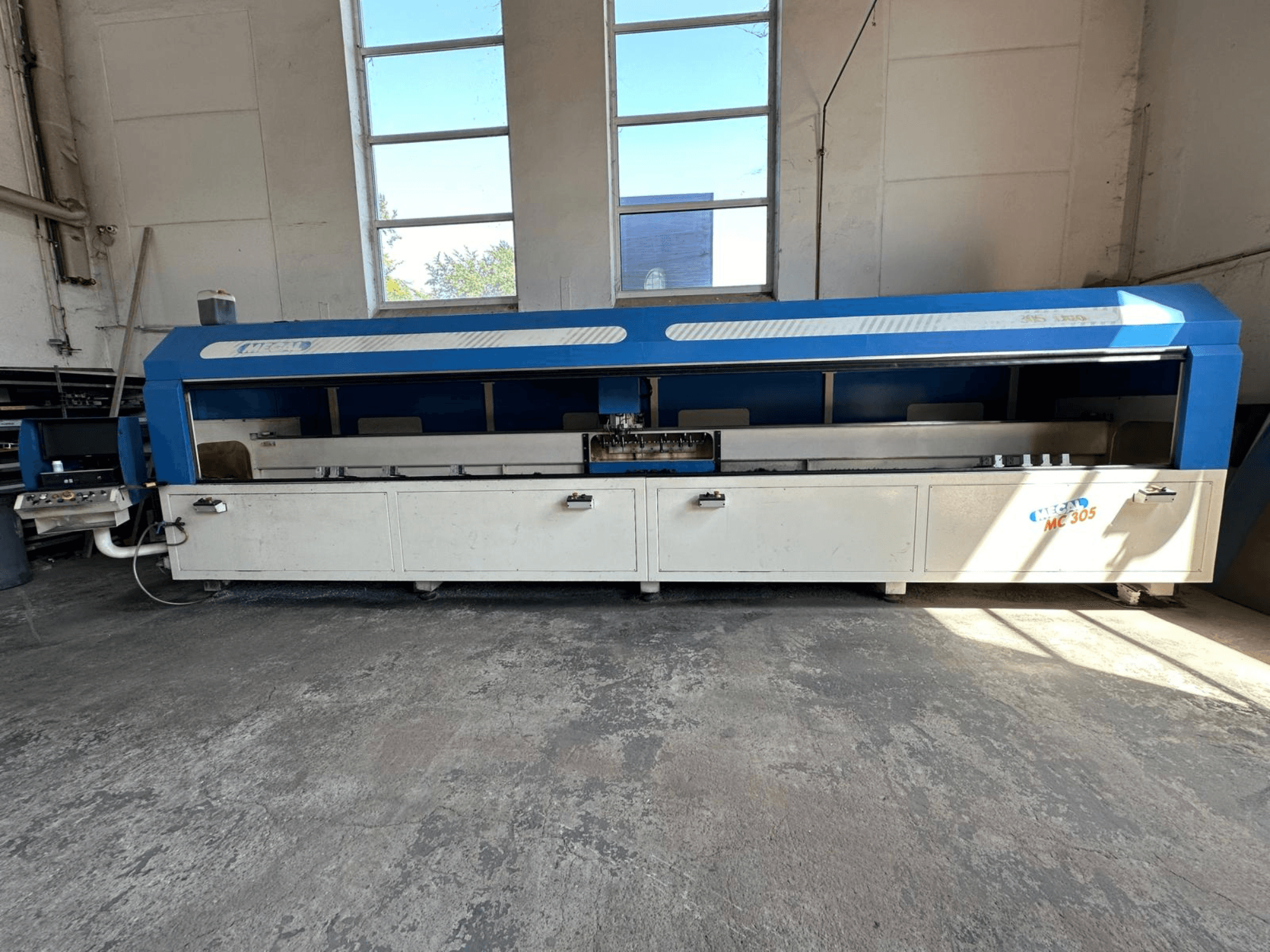 Frontvy av MECAL MC 305 vertikal fleroperationsmaskin med blå och vit design, synligt arbetsbord och kontrollpanel.