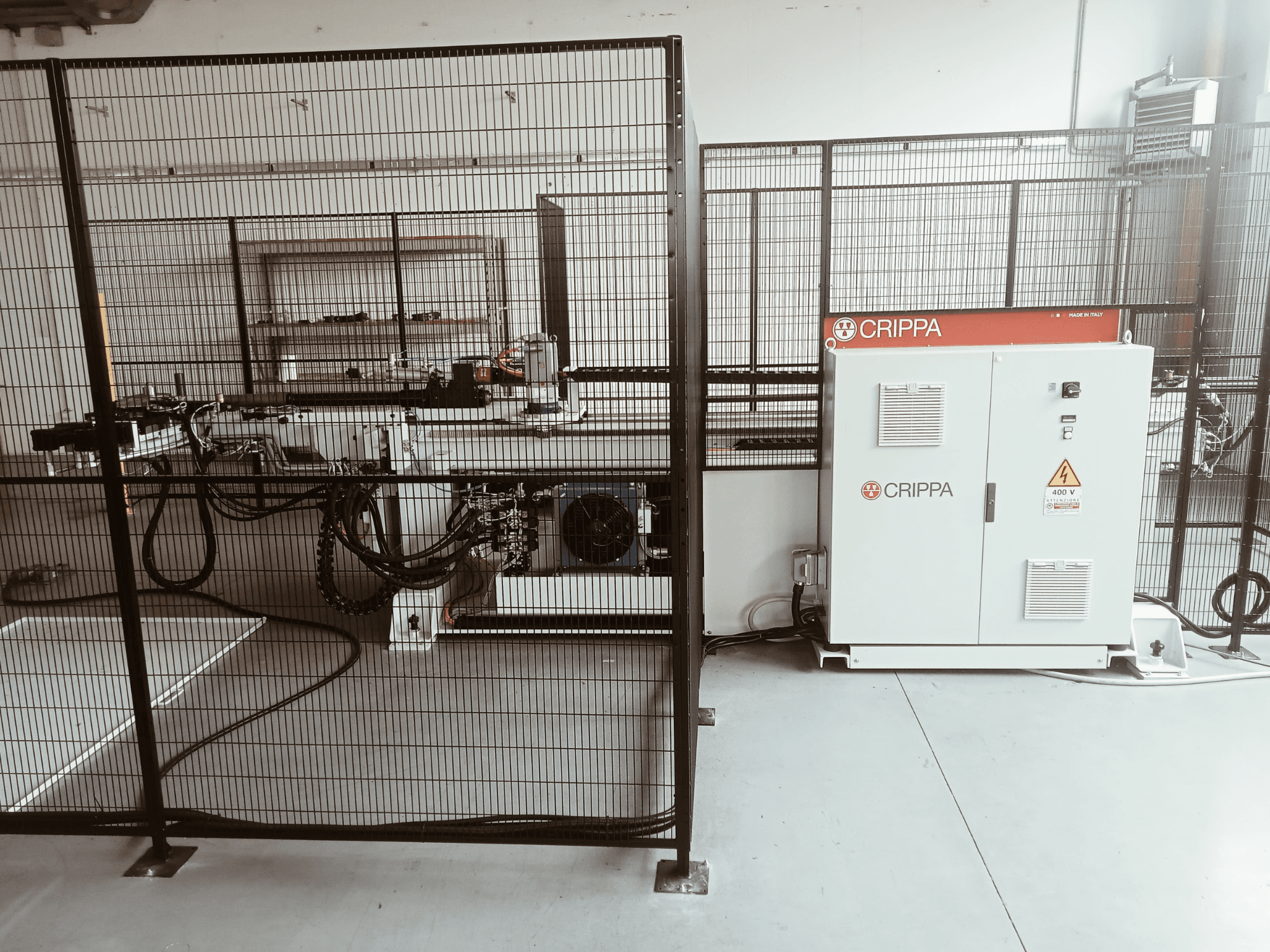 Vit CRIPPA-maskin bakom en säkerhetsbur, med synliga slangar och komponenter, vy från sidan, industrimiljö.