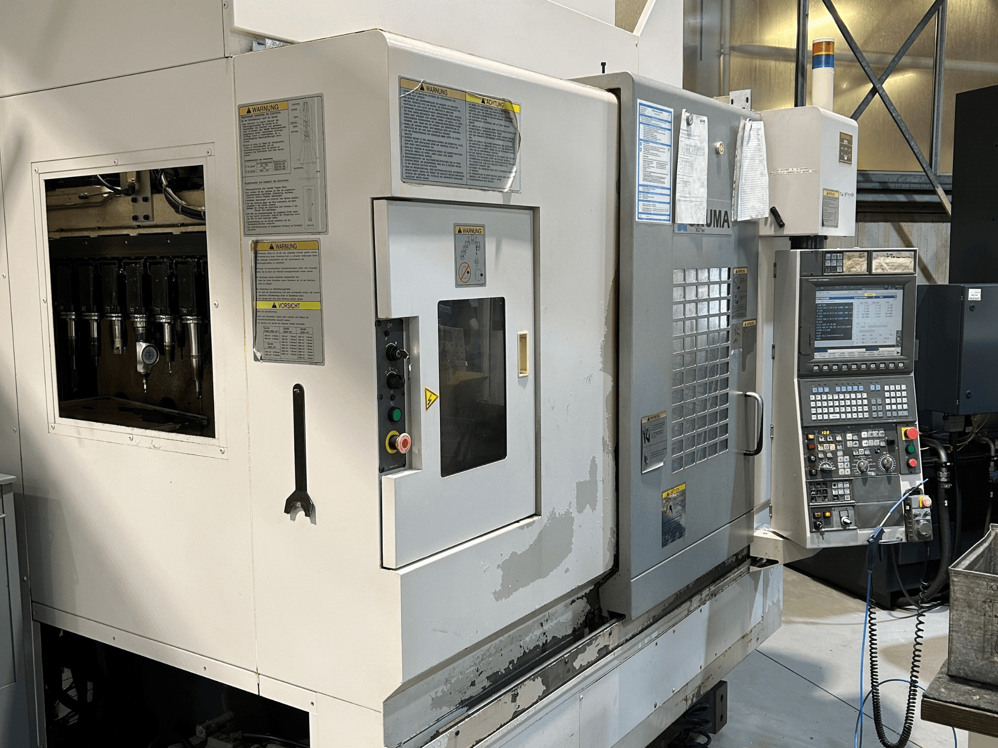 Frontvy av en UMA CNC-maskin med synliga verktygshållare, kontrollpanel, varningsetiketter och manöverknappar.
