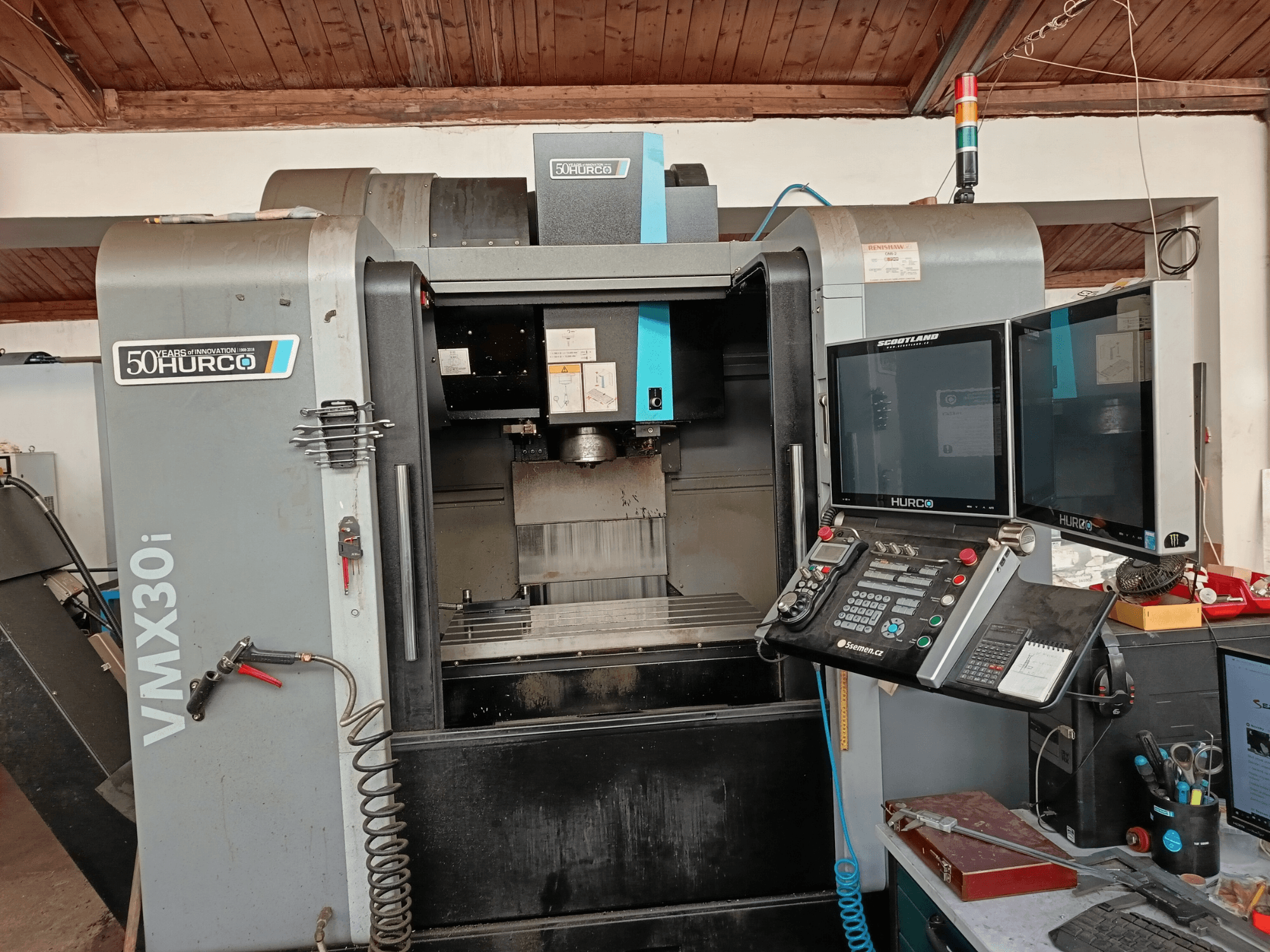Hurco VMX30i CNC-fräsmaskin framifrån, med dubbla bildskärmar, kontrollpanel och en ansluten slang.