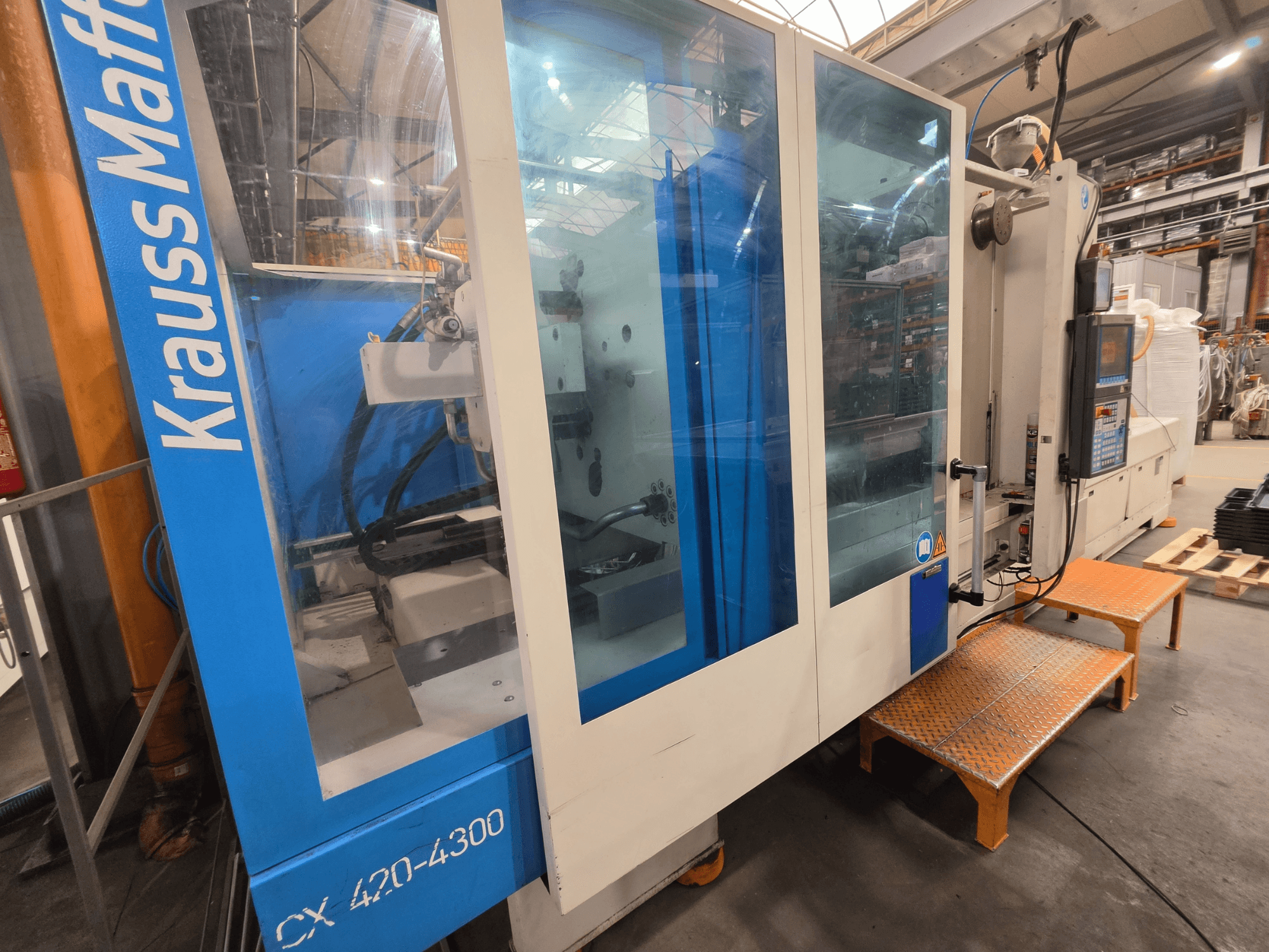 Krauss Maffei CX 420-4300 hydraulisk formsprutningsmaskin, sidovy, med kontrollpanel och transparenta paneler.