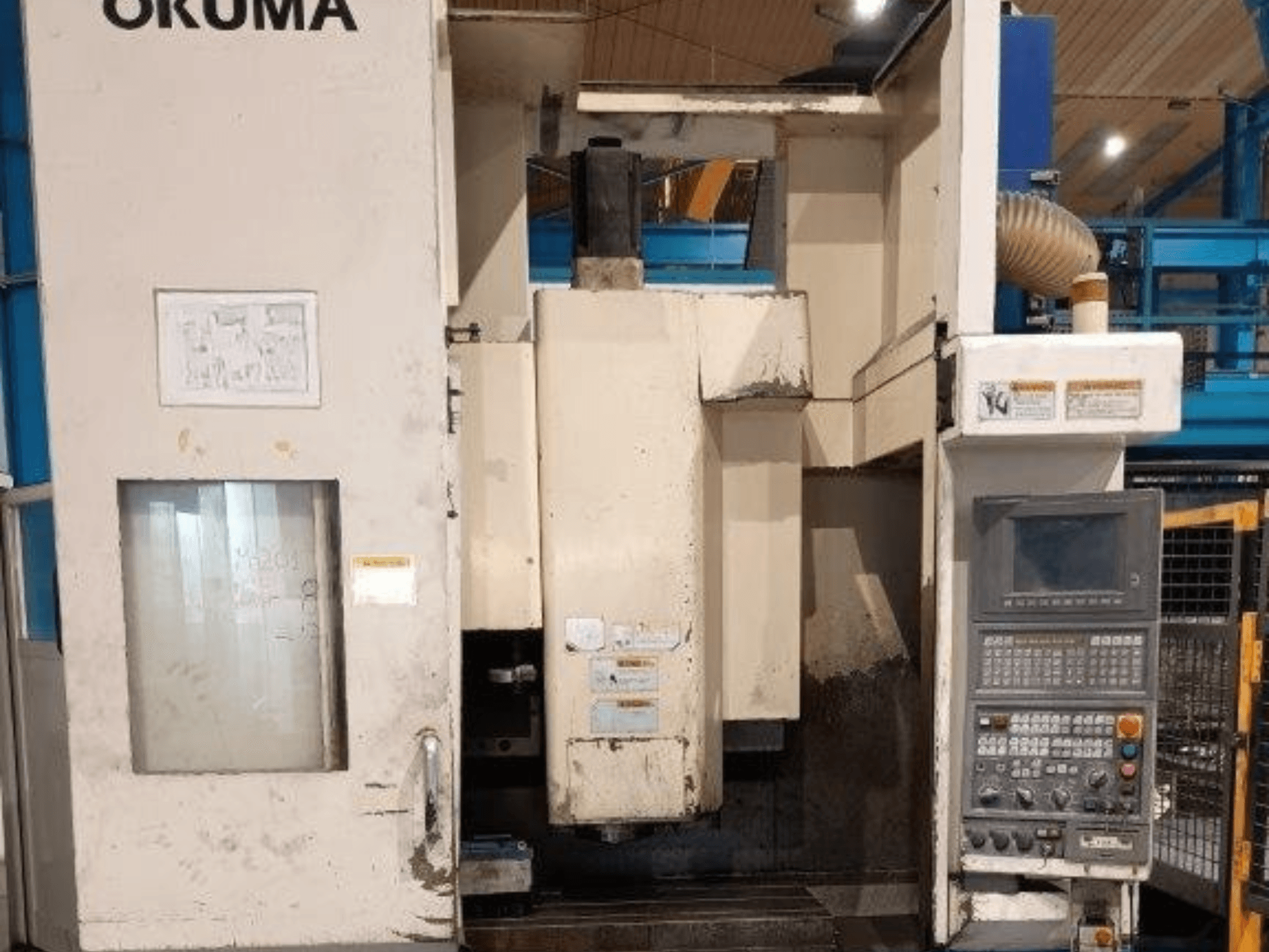 Okuma CNC-fräsmaskin, framifrån, har kontrollpanel med knappar, display och synliga märken på maskinkroppen.