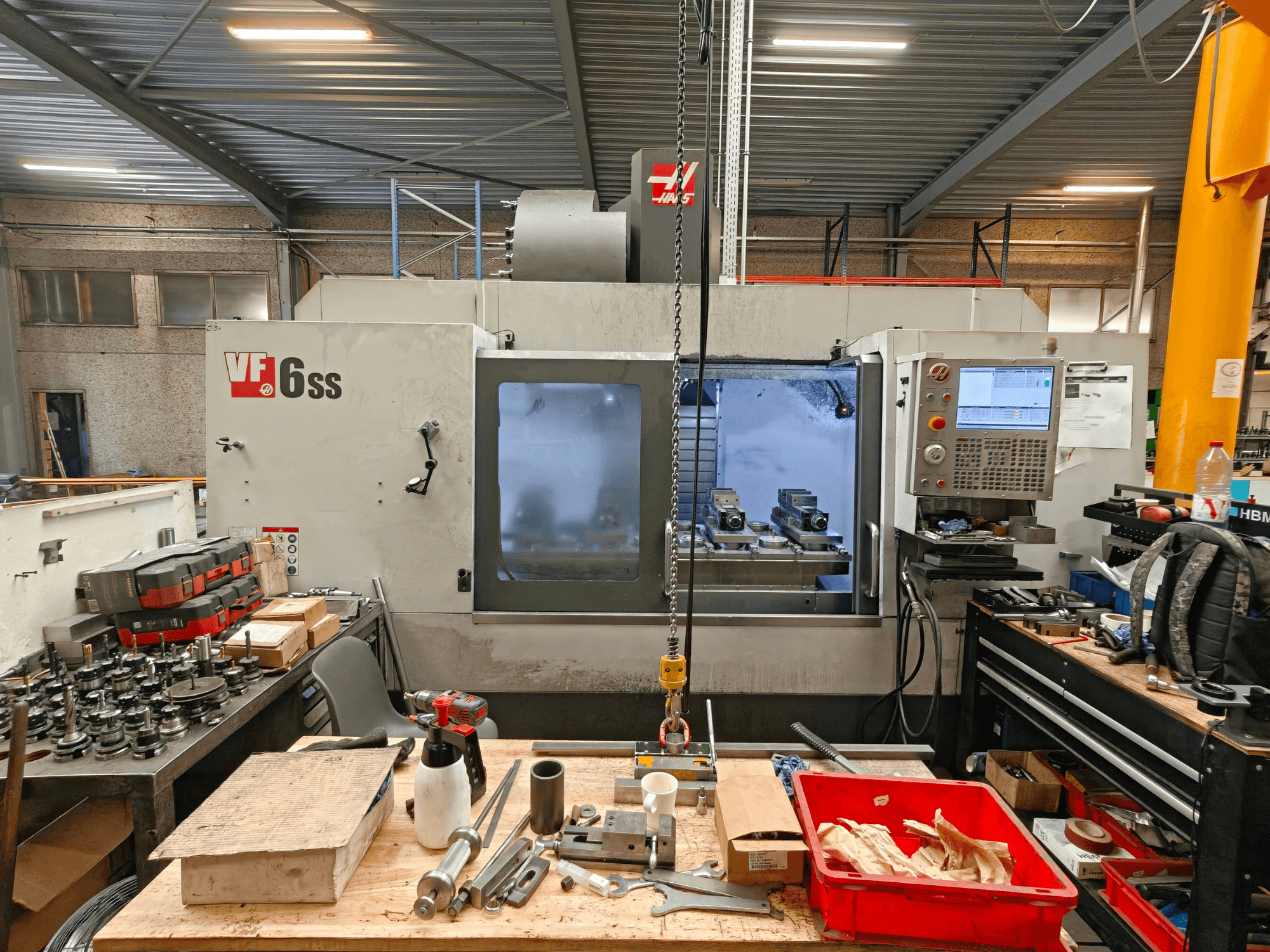 Ett vertikalt bearbetningscenter av typen Haas VF-6SS i en verkstad, sett från sidan, där man ser kontrollpanelen och arbetsytan full av verktyg.