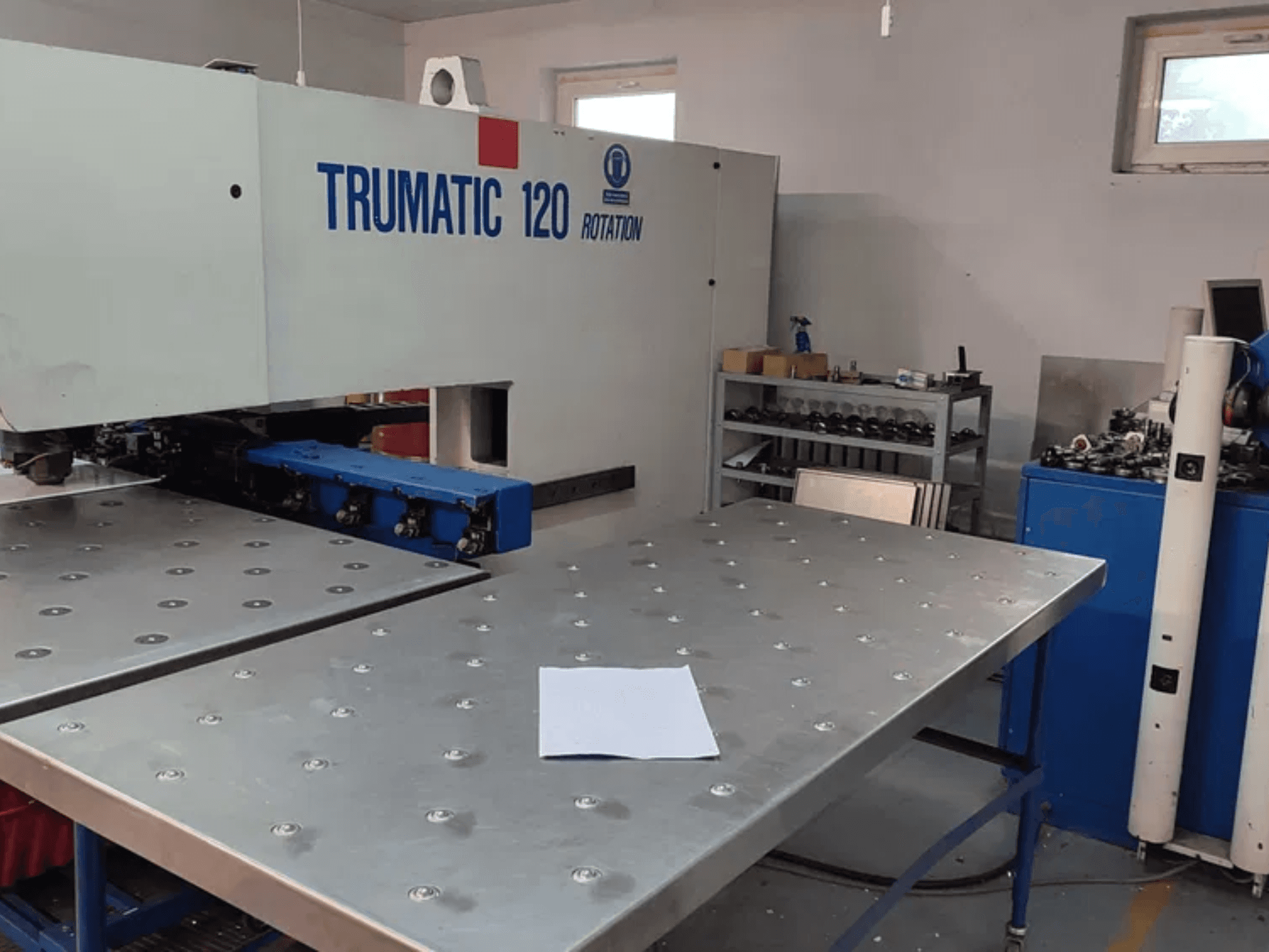 TRUMPF TRUMATIC 120R CNC-stansmaskin sedd framifrån, med ett metallbord med stansade hål och ett tomt ark.