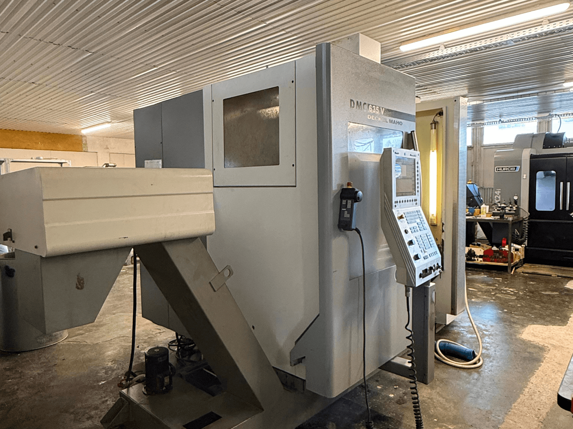 DMC G635V fräsmaskin i en verkstad, vy framifrån med kontrollpanel och anslutna elverktyg synliga.