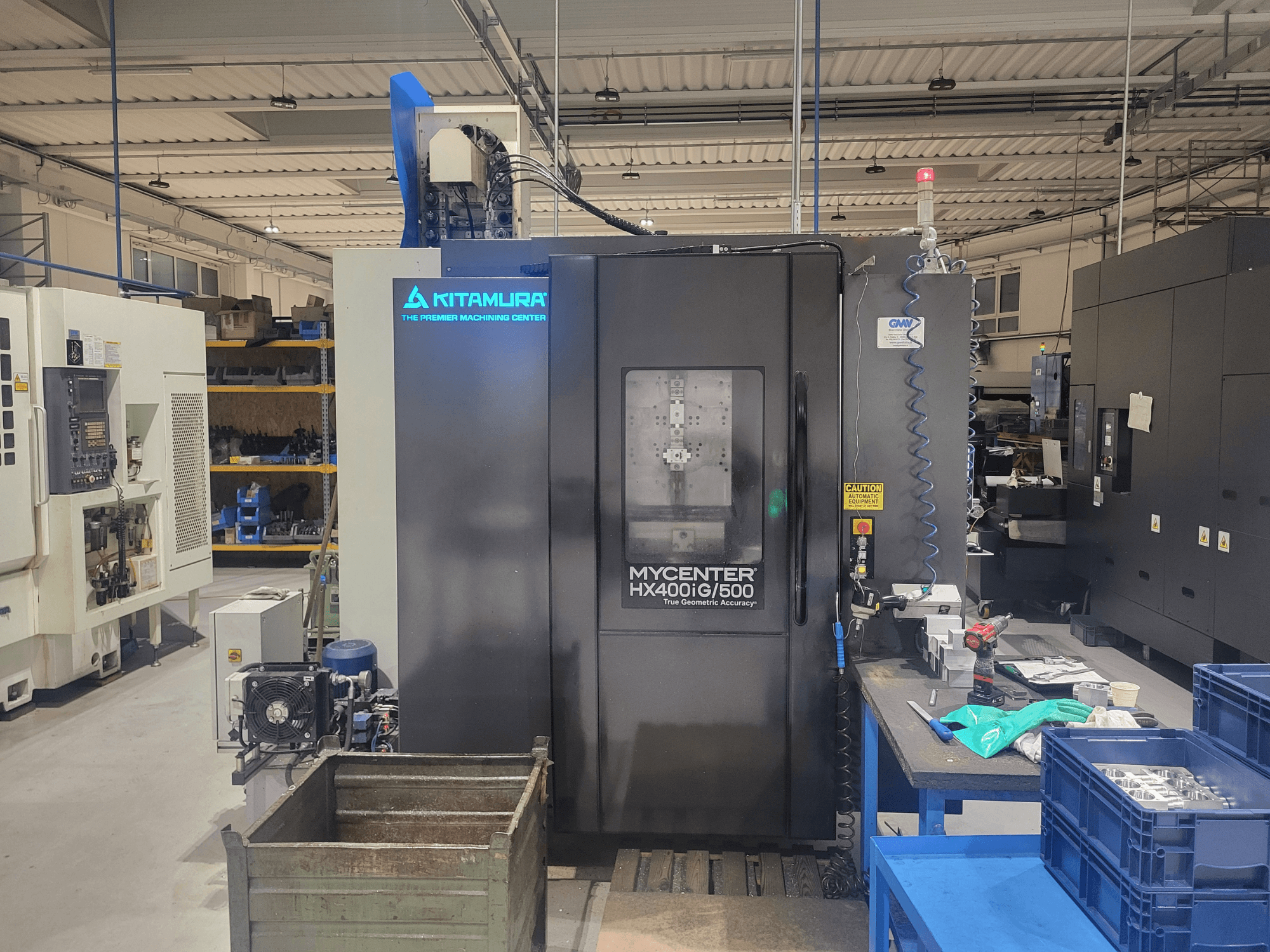 Kitamura Mycenter HX400iG/500 CNC-maskin i en verkstad, vy framifrån, med reglage, verktygsförvaring och material i närheten.