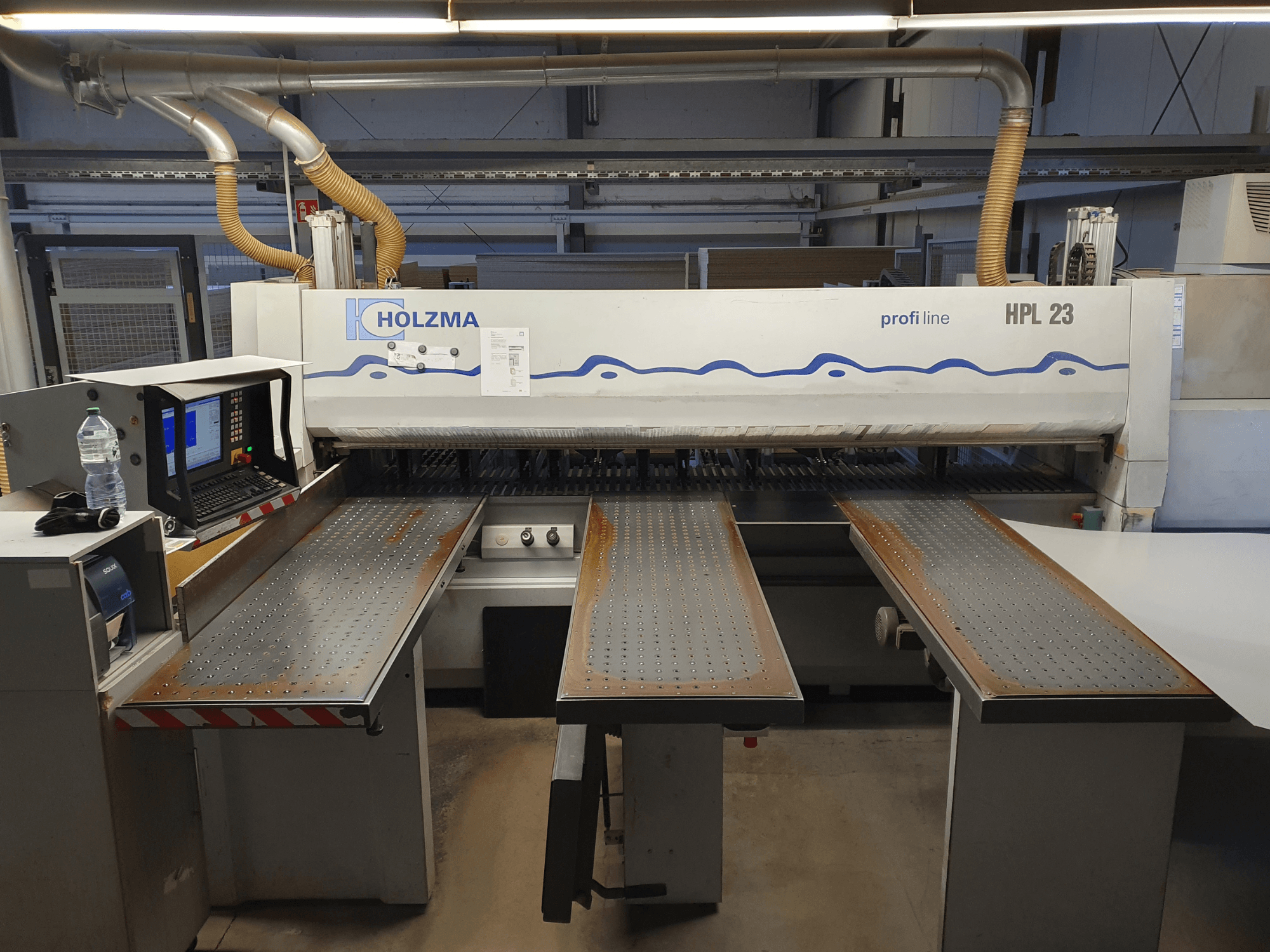 HOLZMA HPL 23 skärmaskin visad framifrån, med tre perforerade bord, datorterminal och vattenflaska i närheten.
