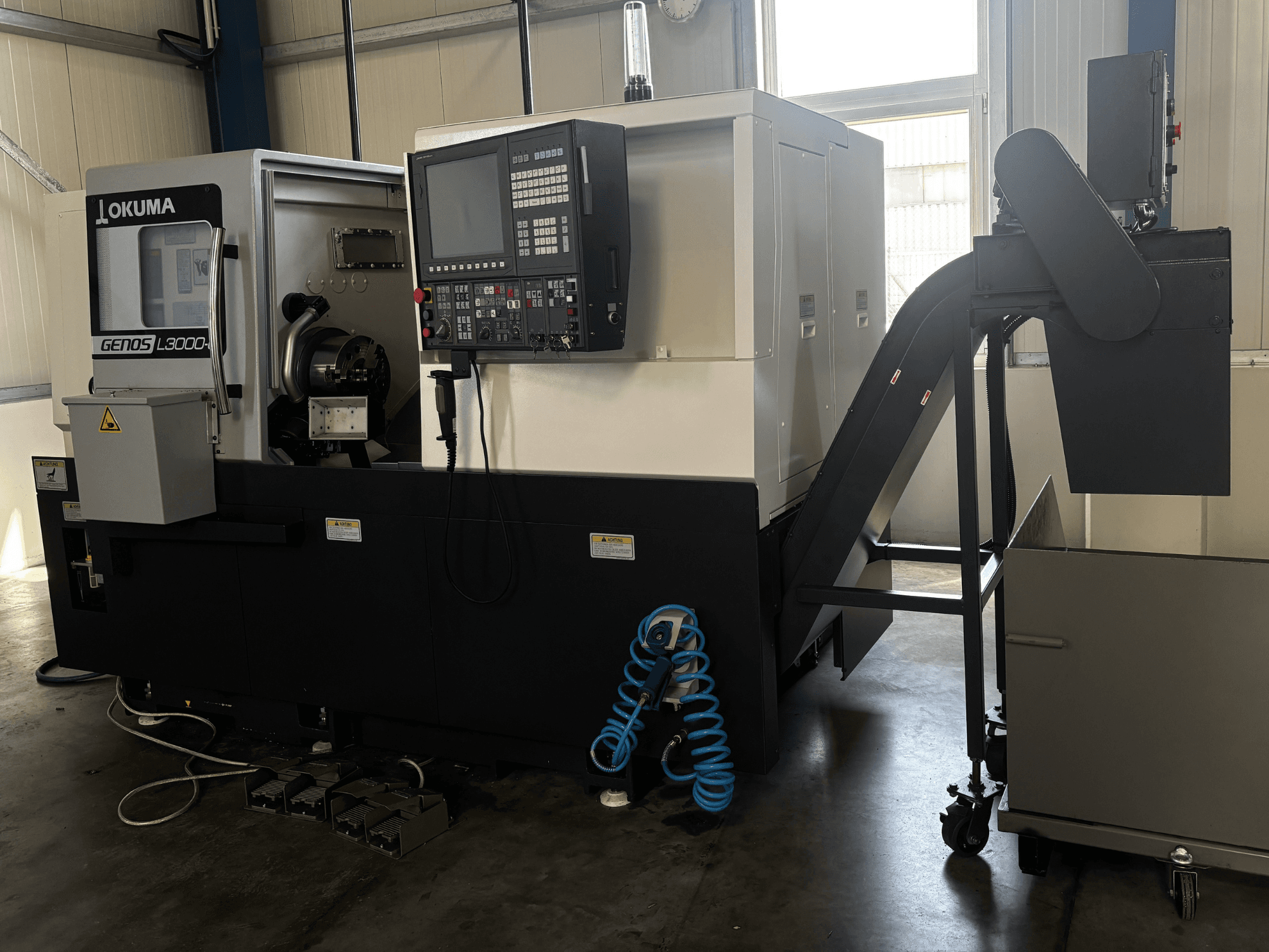 Okuma GENOS L3000-e horisontell svarv, framifrån sett, med kontrollpanel, transportband och synligt spindalområde.