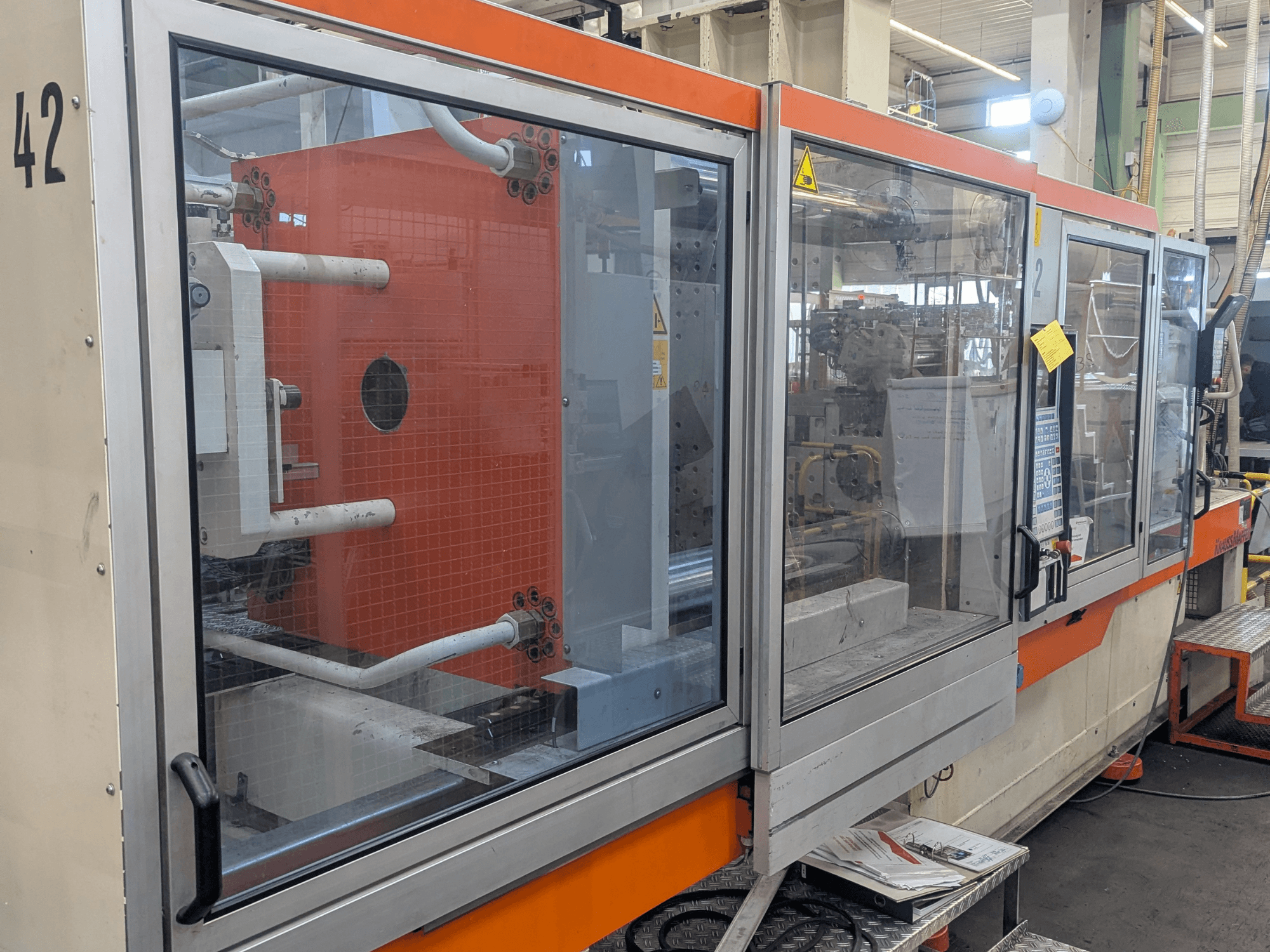 Krauss Maffei KM 350-3000 hydraulisk formsprutningsmaskin, sidovy som visar reglage och interna komponenter bakom glaspanel.