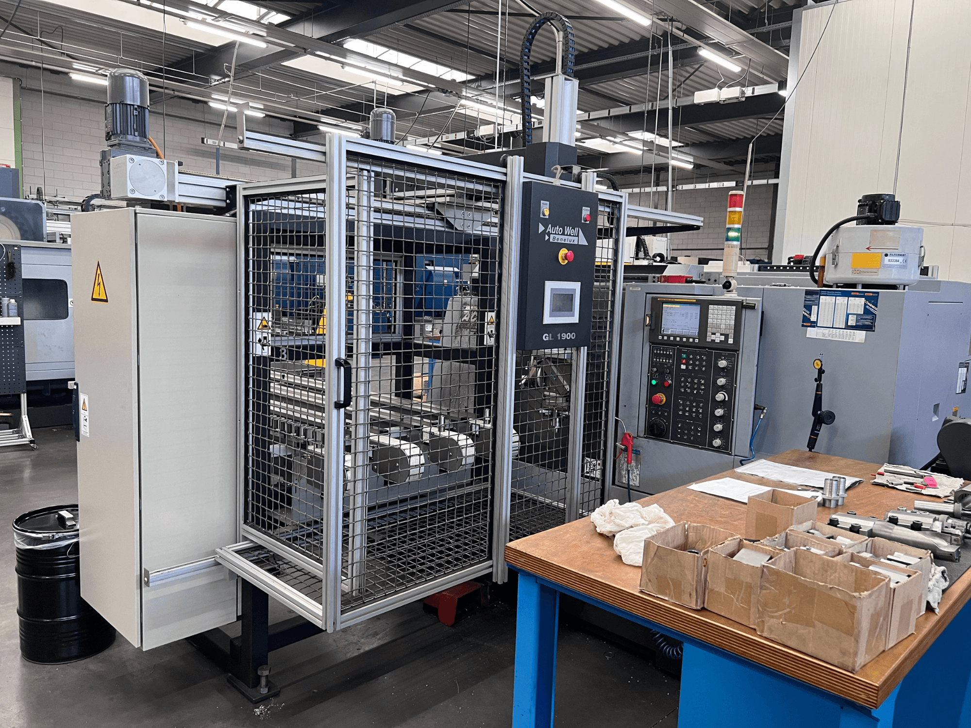 Frontvy av Auto Weld GL 1900-maskin med kontrollpanel, säkerhetsskåp och omgivande verktyg på en arbetsbänk.