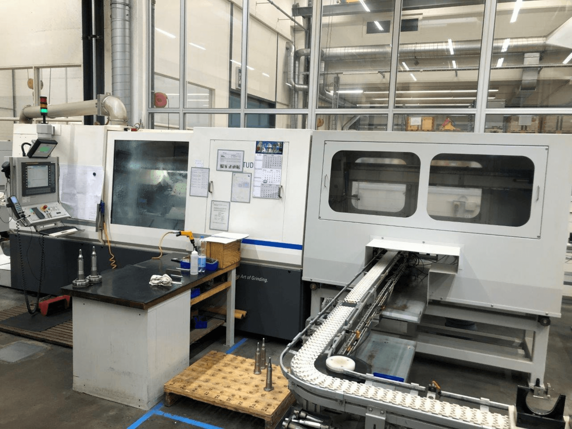 CNC-slipmaskin med kontrollpanel, framifrån; har en transportör och tydliga visningsfönster som visar upp precisionsverktyg.