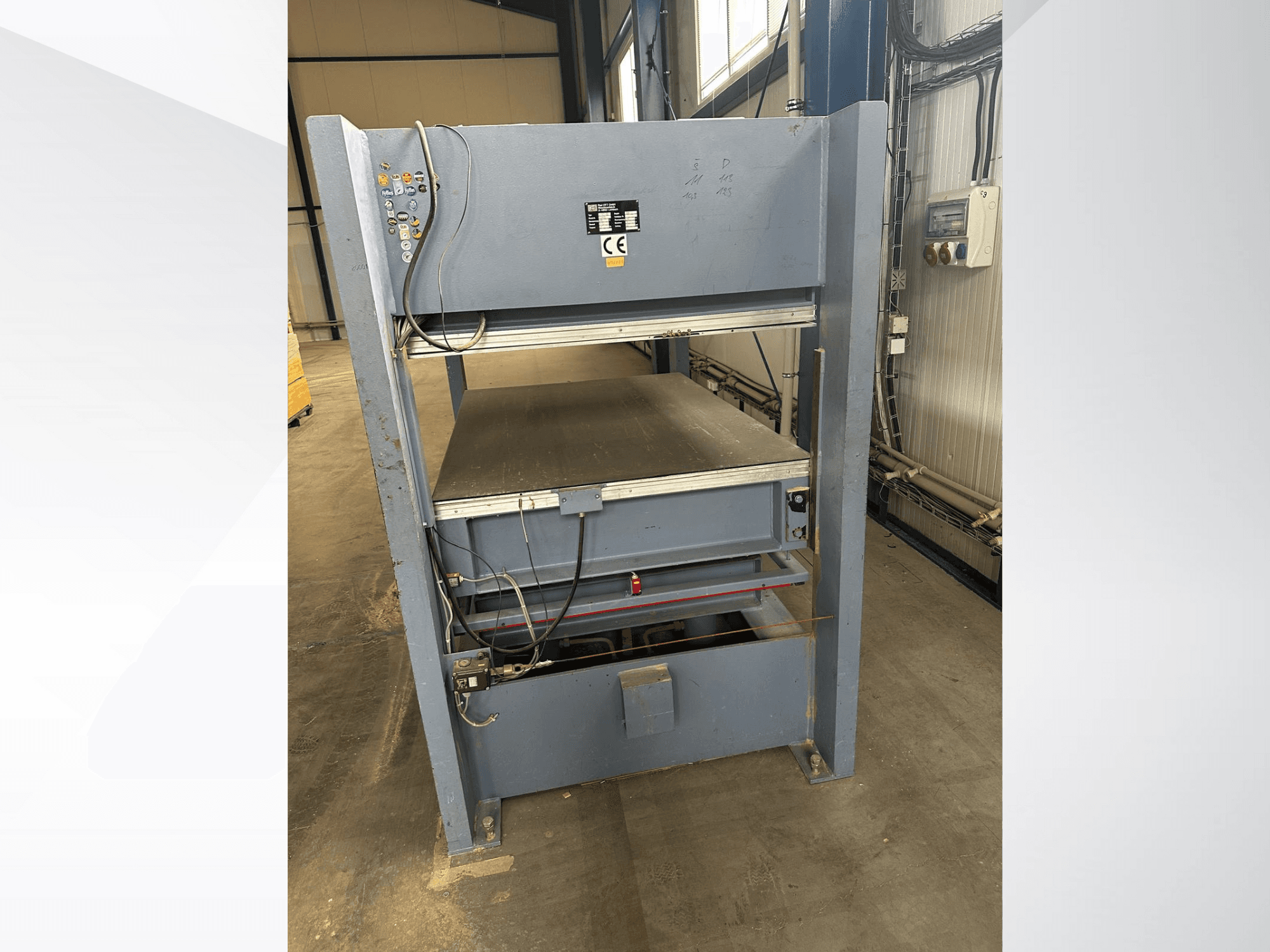 Grå industrimaskin med kontrollpanel, sedd framifrån; inkluderar justerbara plattformar och säkerhetsmarkeringar.