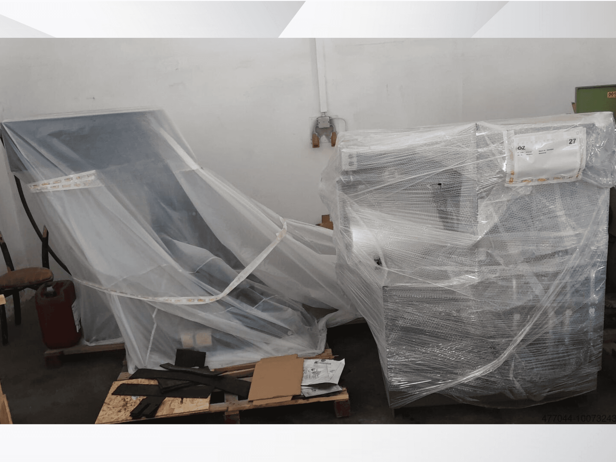 Inslagen industriutrustning i plast, med en stol och en maskin, sedd från en sidovinkel i en lagerlokal.