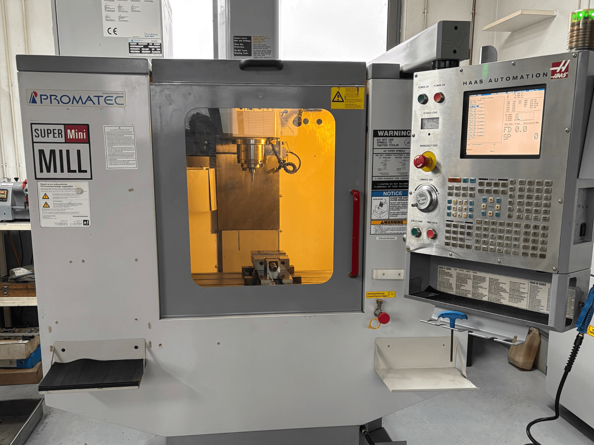 Promatec Super Mini Mill framifrån, utrustad med en Haas Automation-kontrollpanel och synligt skärverktyg inuti.