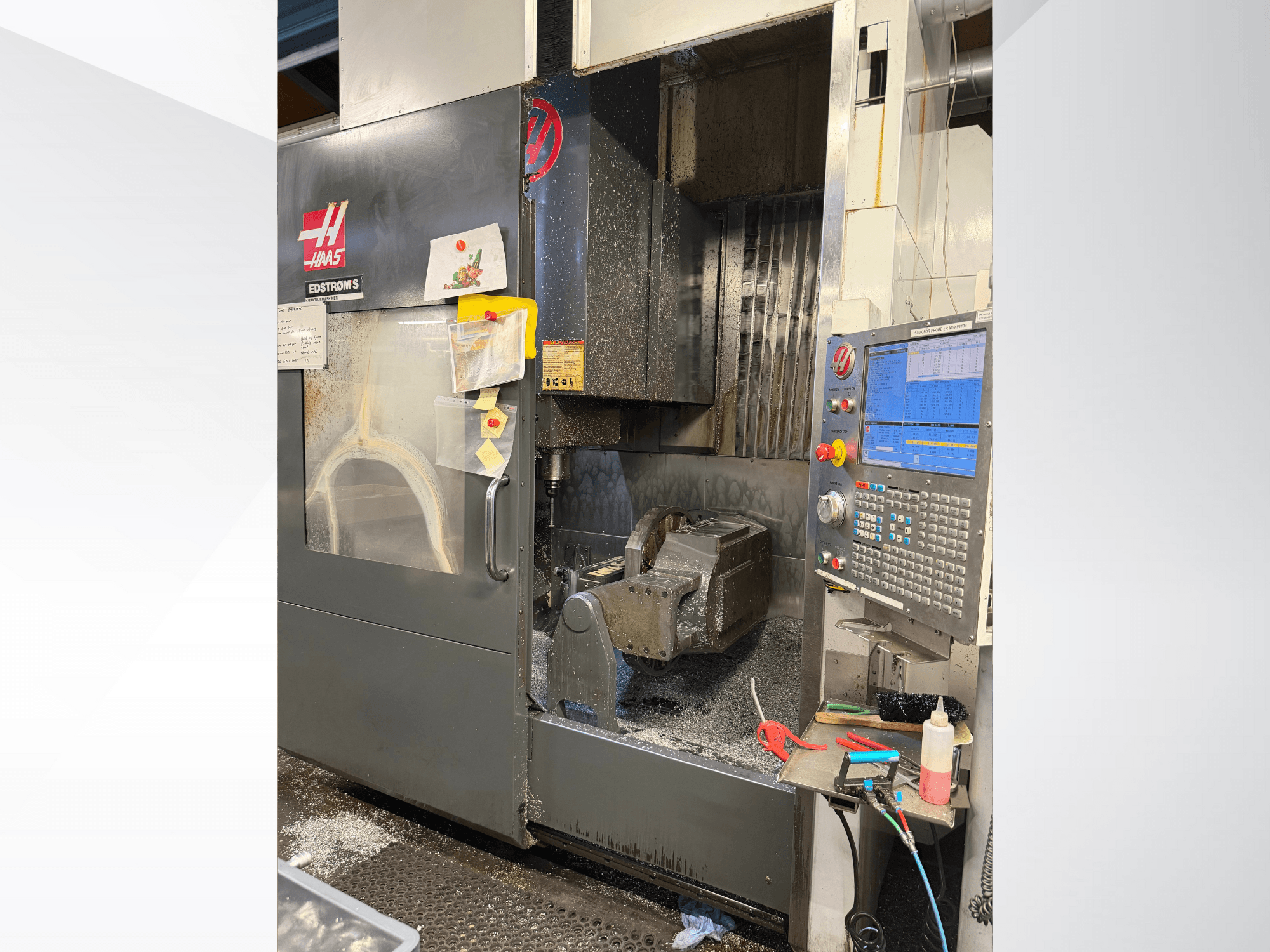Haas CNC-maskin modell EDSTROM S, framifrån, visar arbetsstycke av metall, kontrollpanel och metallspån inuti.