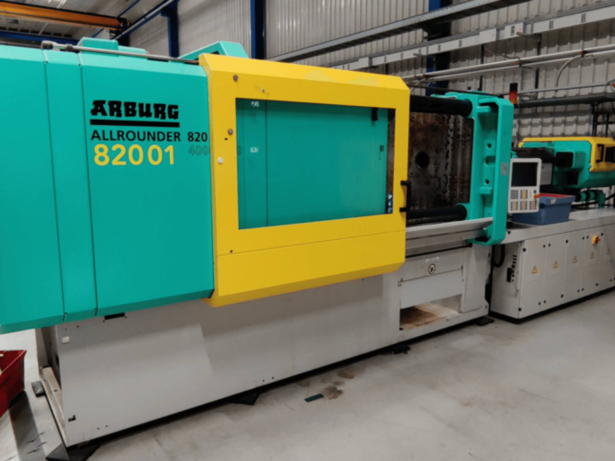 Arburg ALLROUNDER 82001 formsprutningsmaskin i teal och gult, sidovy som visar kontrollpanel och driftsfunktioner.