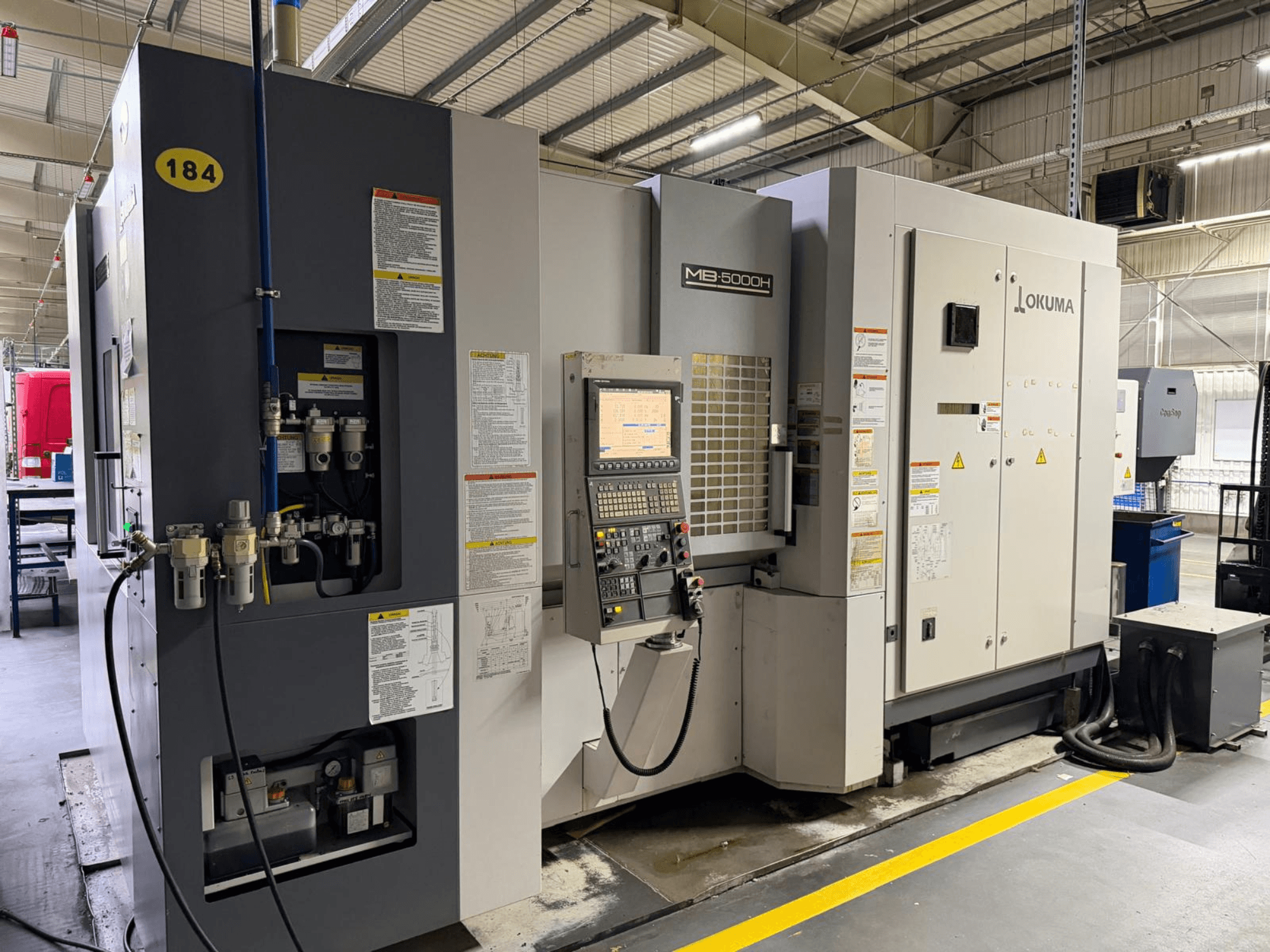 Okuma MB 5000H horisontell bearbetningscenter framifrån, med reglage, märkning och hydraulanslutningar.