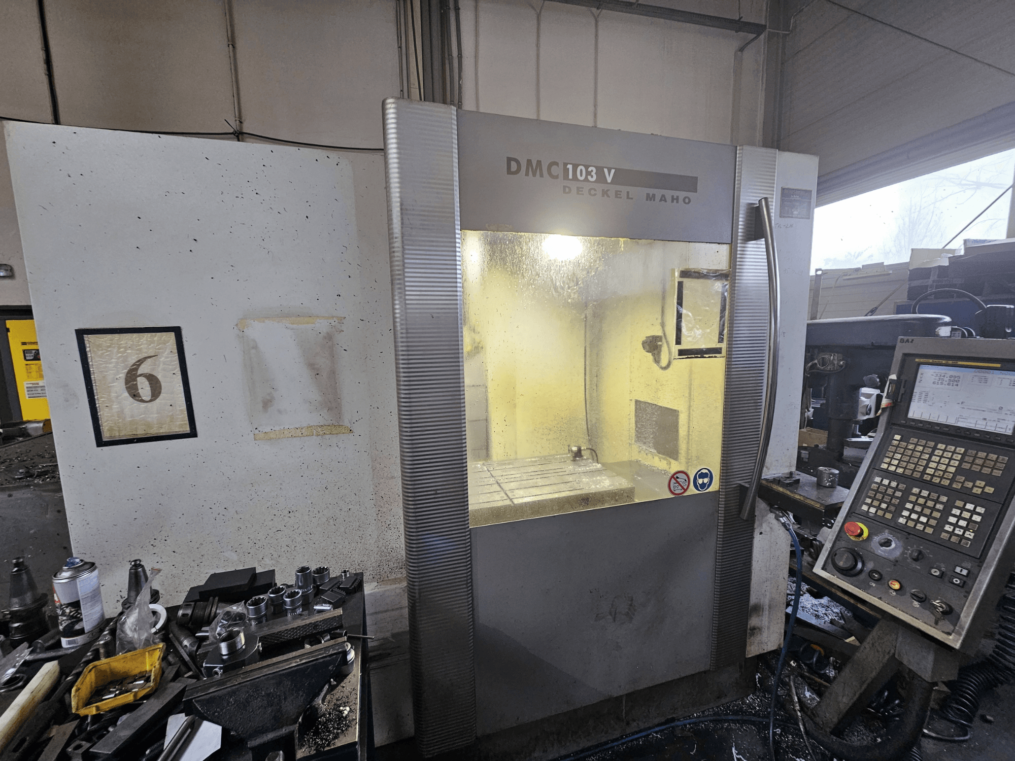 Frontvy av en Deckel Maho DMC 103 V CNC-maskin, som visar kontrollpanelen, arbetsområdet och nummerindikatorn "6".