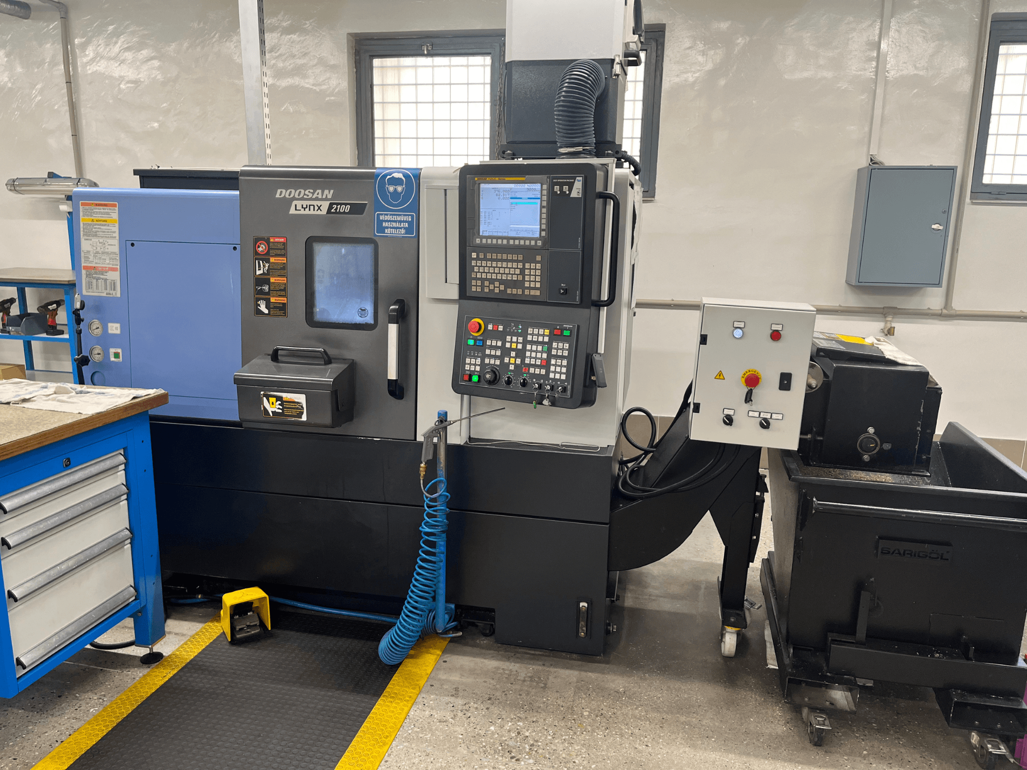 Doosan Lynx 210 svarv i verkstad, med kontrollpanel, verktygsförvaring och kylsystem, sidovy med detaljer om arbetsytan.