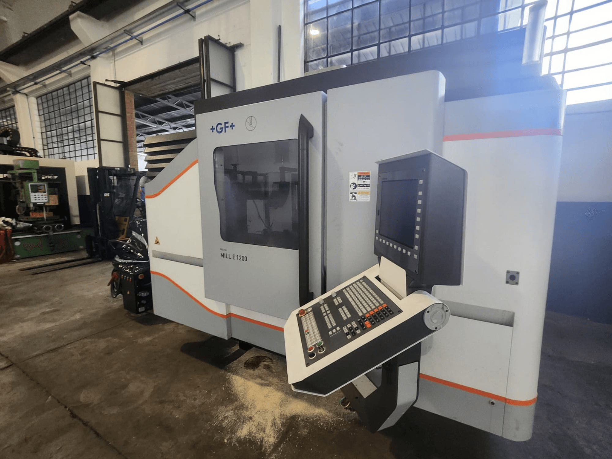 GF MILL E1200, främre vy av fräsmaskin med kontrollpanel, displayskärm och säkerhetsetiketter, i verkstadsmiljö.