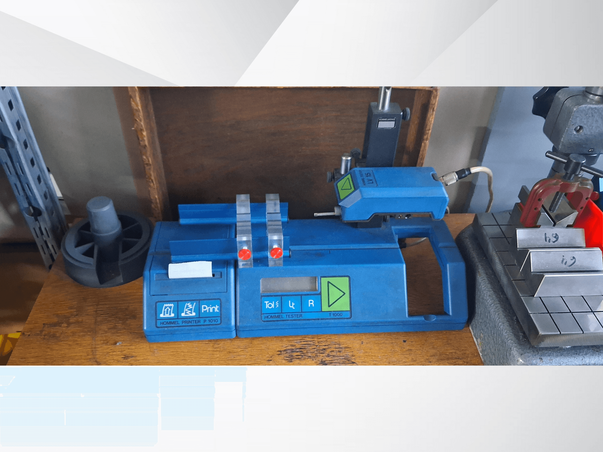 Blå Hommel T 1000-skrivare och T 1 010-testare med röda knappar, sett framifrån på en arbetsbänk med metallblock.