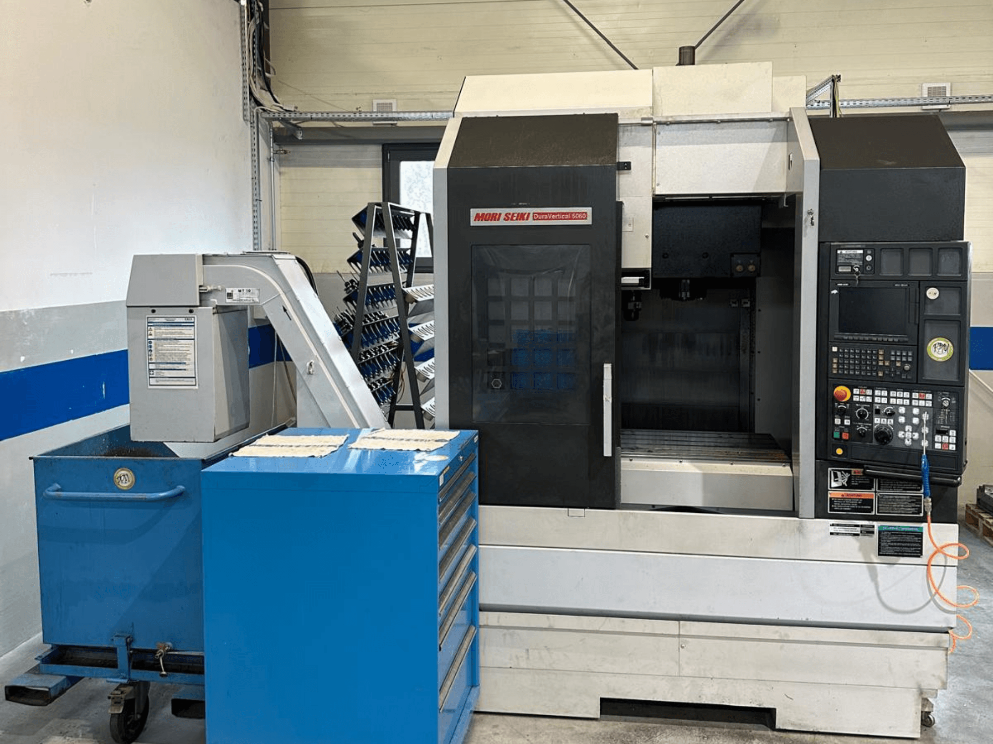 MORI SEIKI DURA VERTICAL 5060, framifrån sett: ett vertikalt bearbetningscenter med kontrollpanel och verktygsförvaring i närheten.
