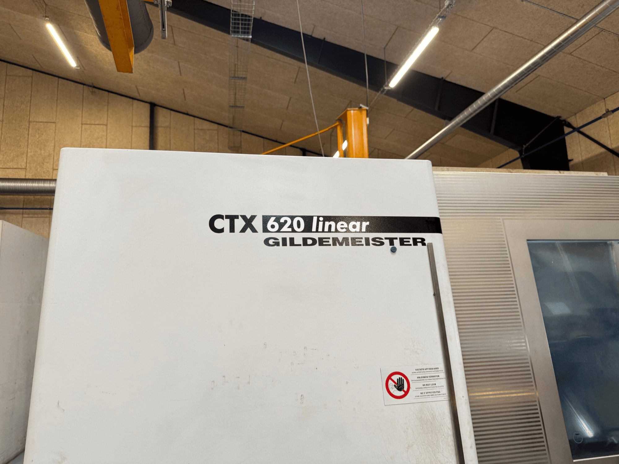 CTX 620 Linear Gildemeister-maskinens sidovy, med vit utsida och varningsetiketter för säkerhet.