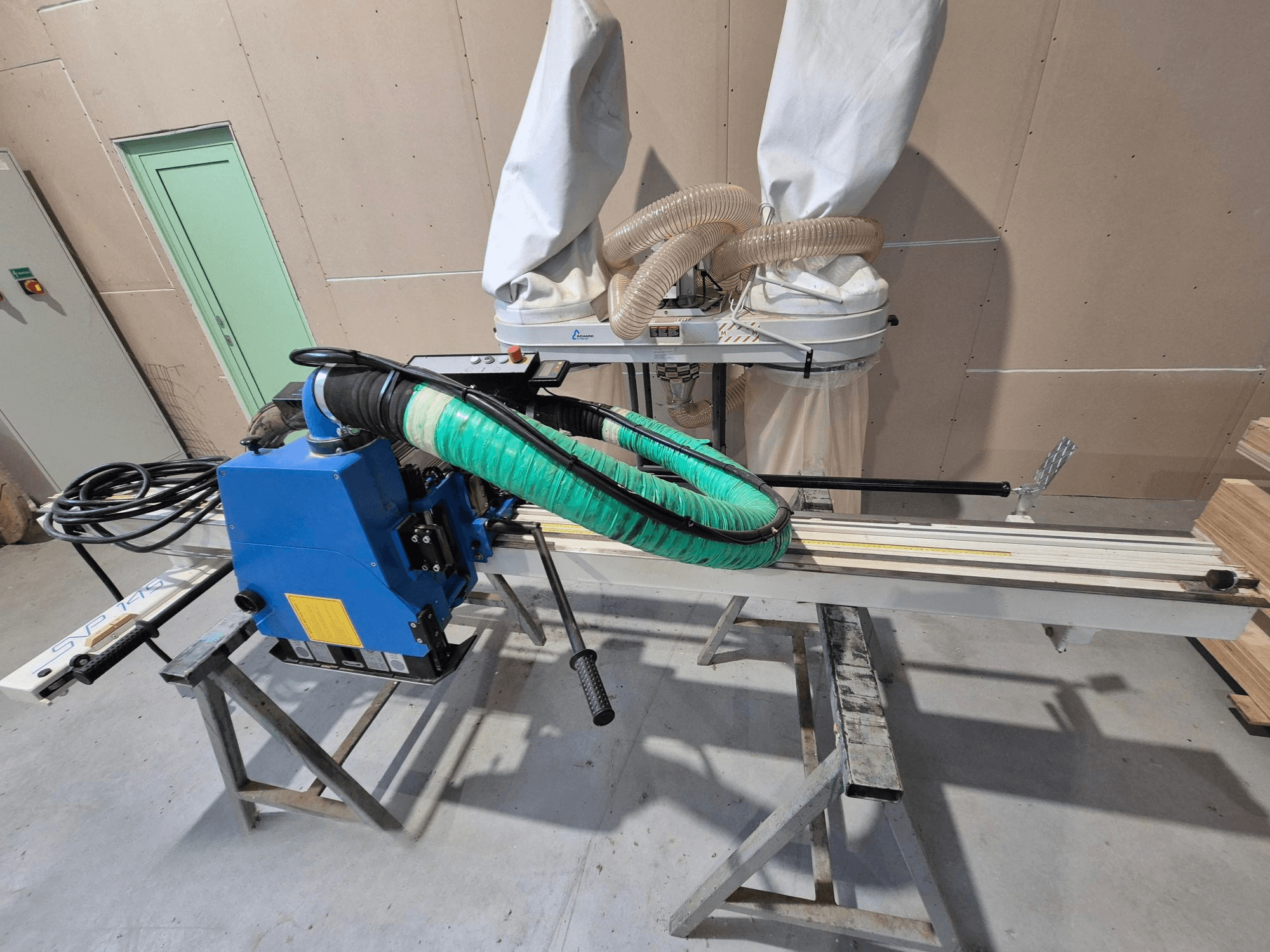 Blå SVP-175 horisontell panelsåg med grön dammslang och stöd, sedd från sidan i en verkstadsmiljö.