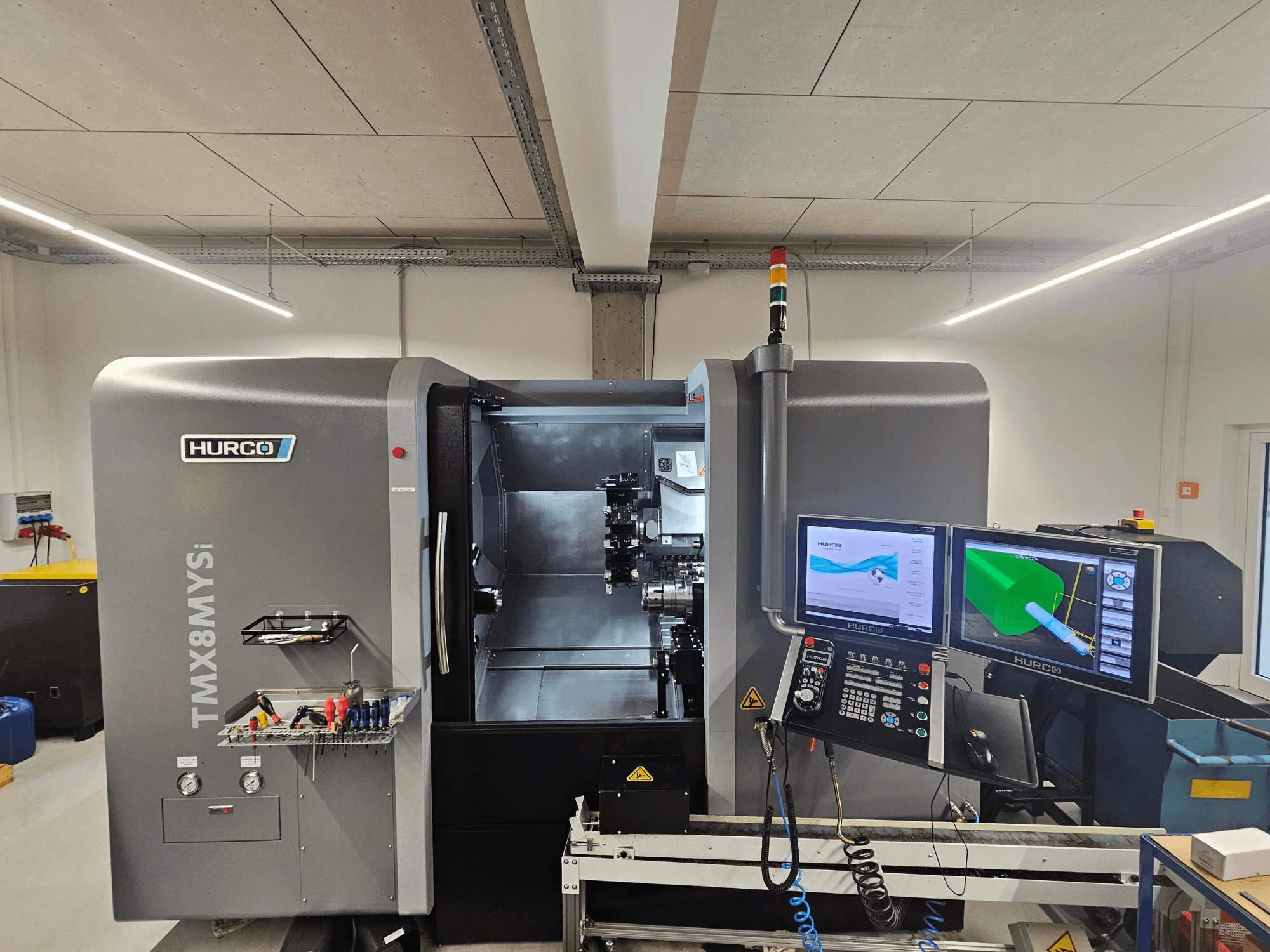 Hurco TMX 8 MYSi svarvfräs i en verkstad, med dubbla bildskärmar, kontrollpanel och verktyg på sidan.