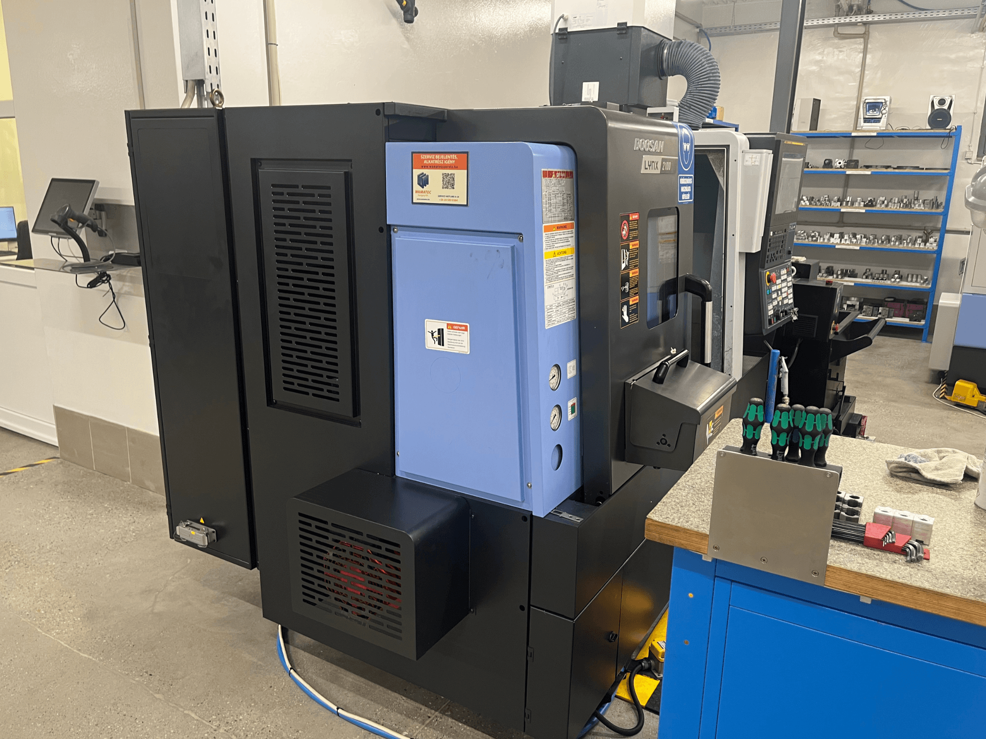 Doosan Lynx 2100 svarv, sidovy, visar kontrollpanel, ventilationssystem och verktyg på en arbetsbänk.