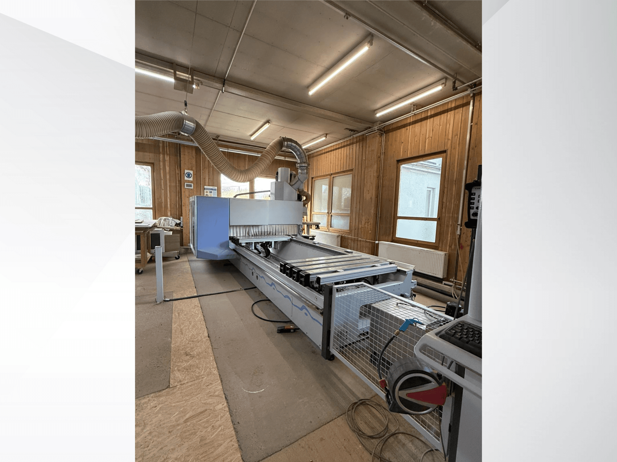 CNC-fräsmaskin i en verkstad, vy från sidan, med en stor blå kropp, monterad bandtransportör och synlig kontrollpanel.