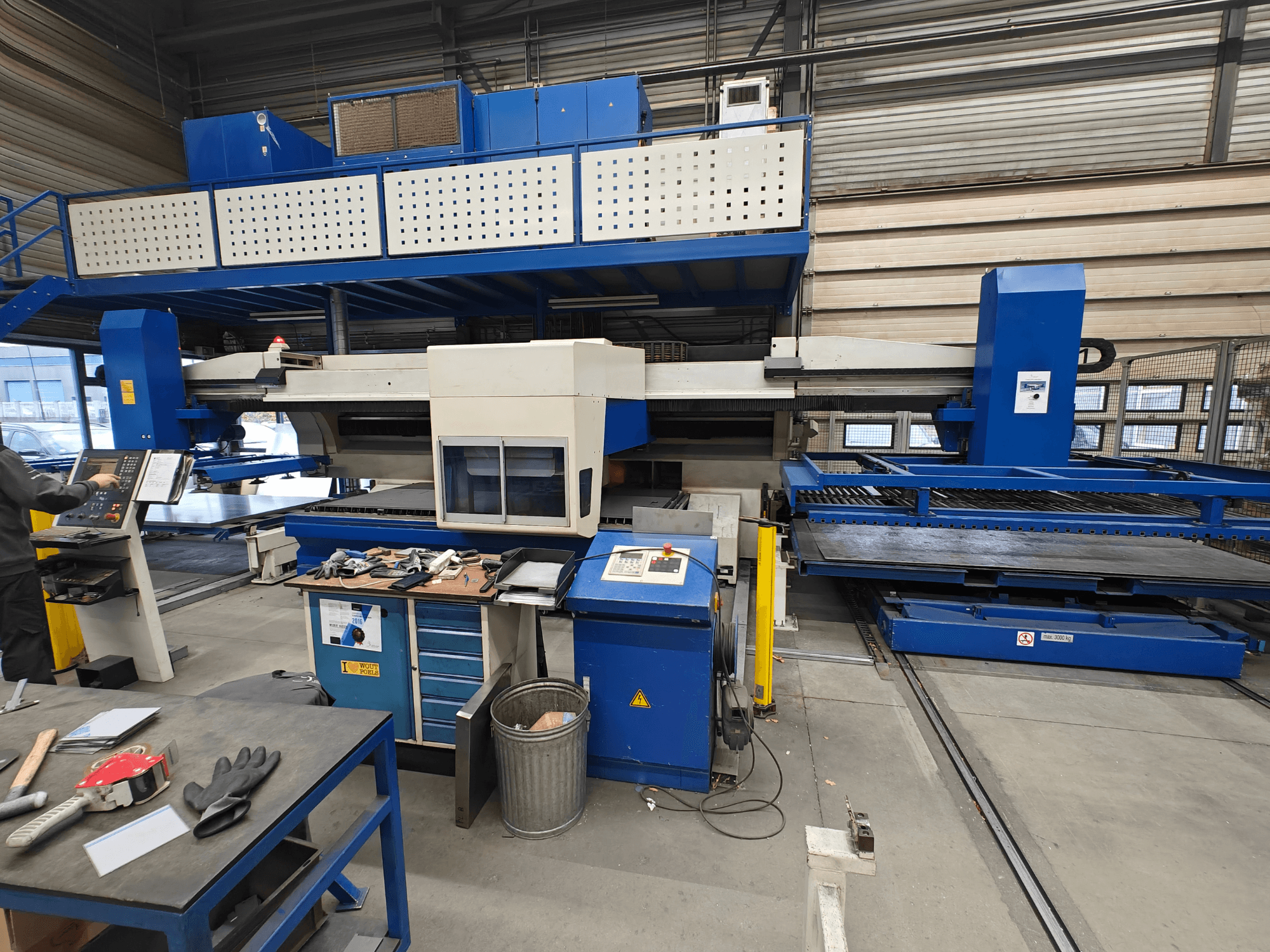 Industriell CNC-maskin framifrån, med blå och vit konstruktion, kontrollpanel och olika verktyg på arbetsbordet.
