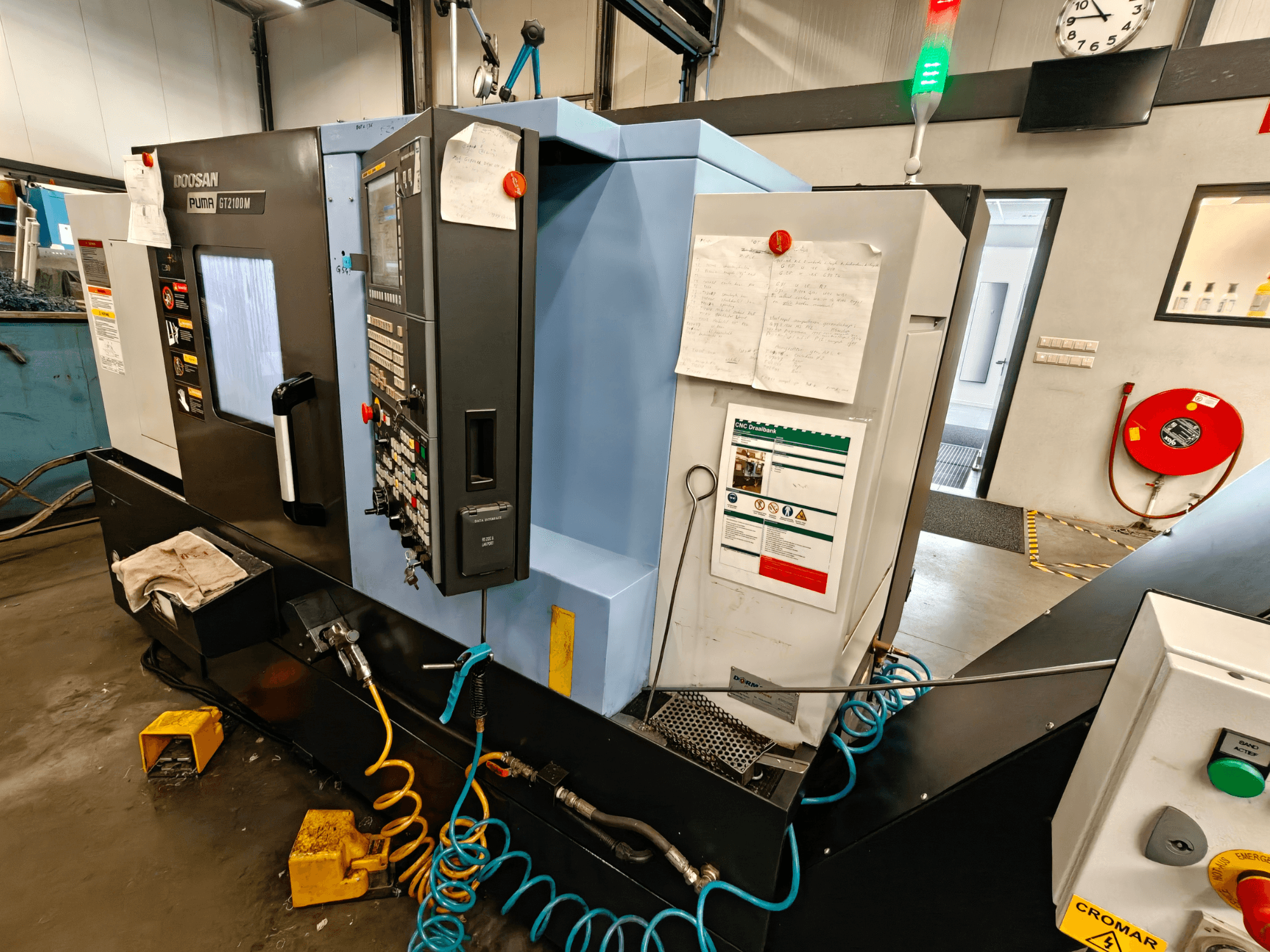 Frontvy av DOOSAN Puma GT 2100M horisontell svarv med kontrollpanel, säkerhetsfunktioner och underhållsanvisningar synliga.