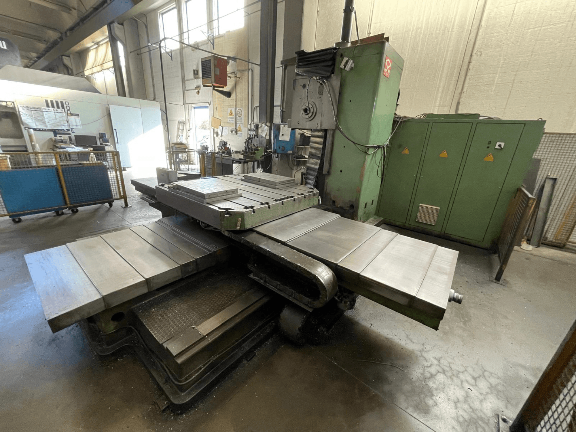Stor industriell fräsmaskin med grön kaross, vy från sidan, med flera plana ytor och förvaringsskåp i bakgrunden.