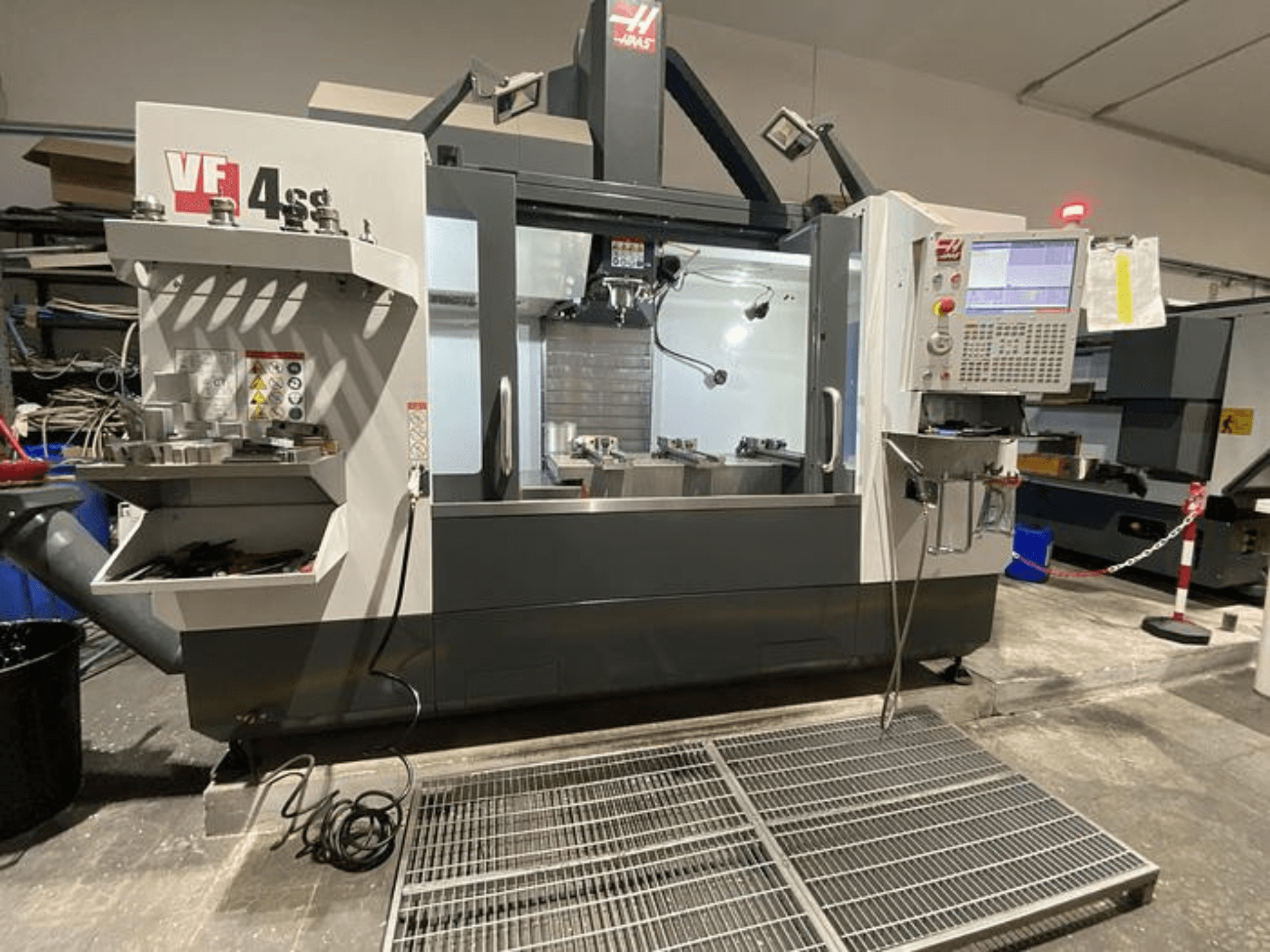 Haas VF-4SS CNC-fräsmaskin, framifrån, med verktygsförvaring, kontrollpanel och synligt arbetsområde i en verkstadsmiljö.