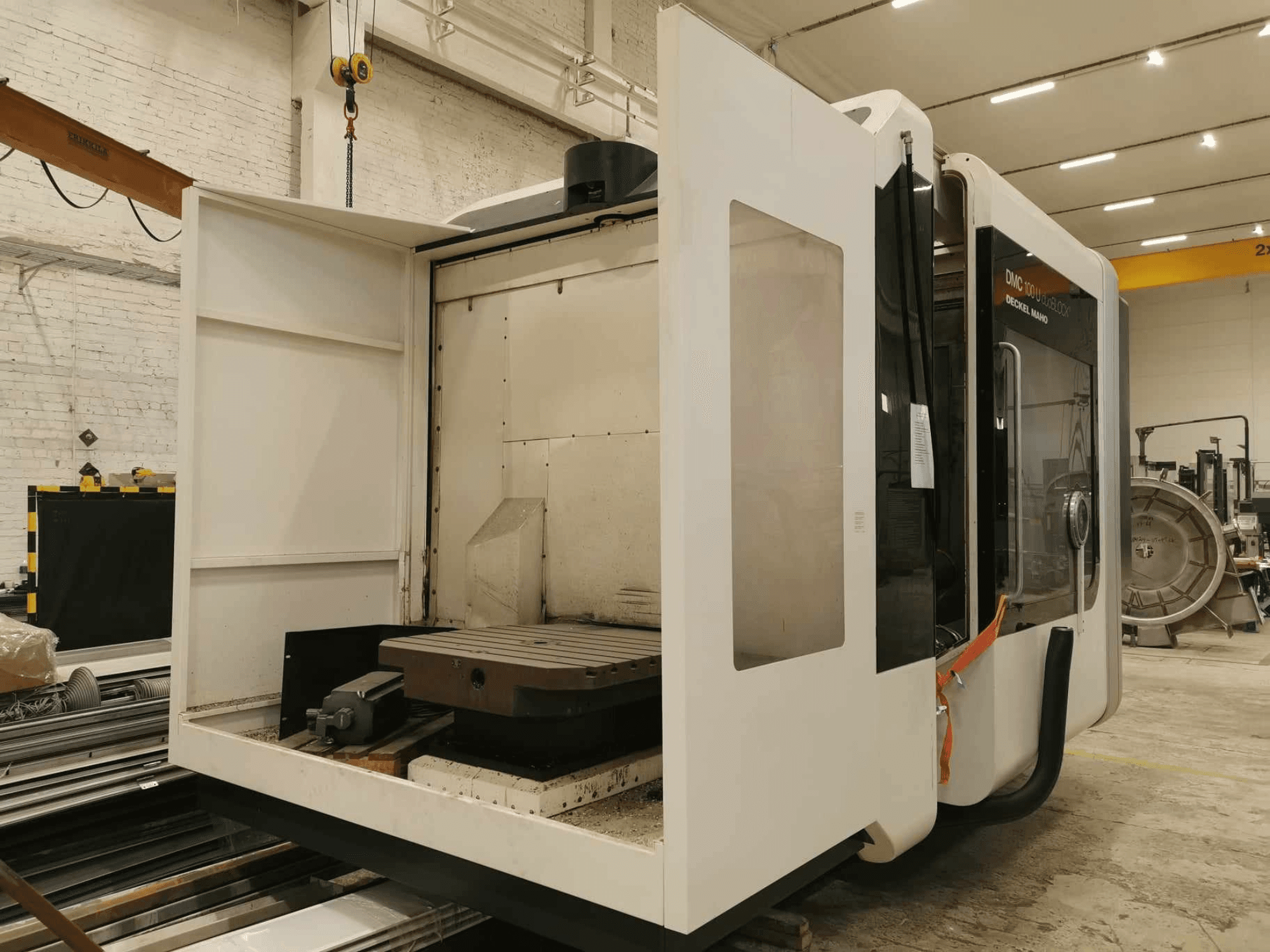 DMC 100U linjär CNC-maskin, sidovy med öppen åtkomstdörr, visar arbetsbord och interna komponenter.