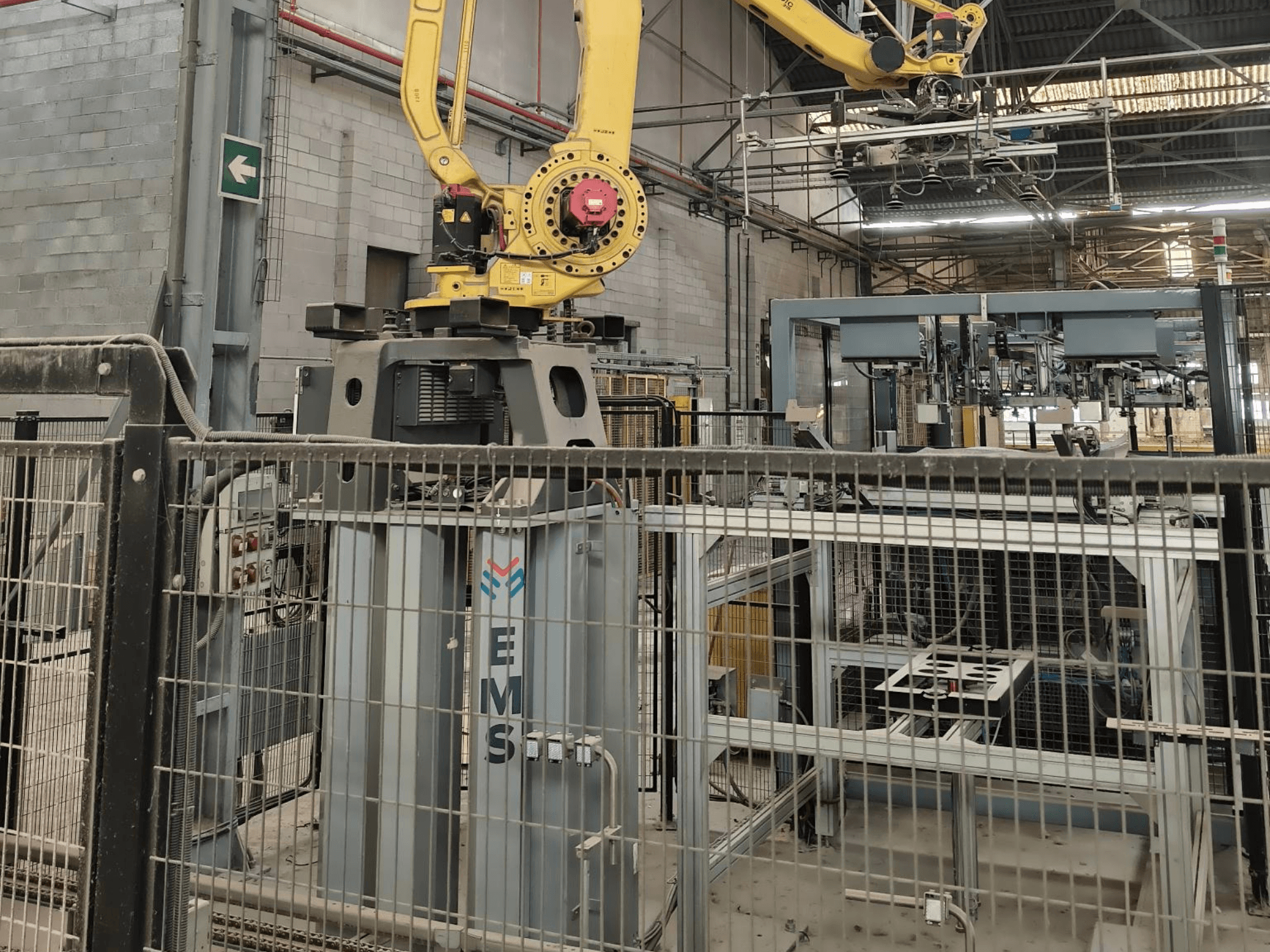 Framifrån sett: en FANUC M-410iC/315-robotarm placerad ovanför ett EMS-verktyg, med industriutrustning och skyddsstängsel i bakgrunden.