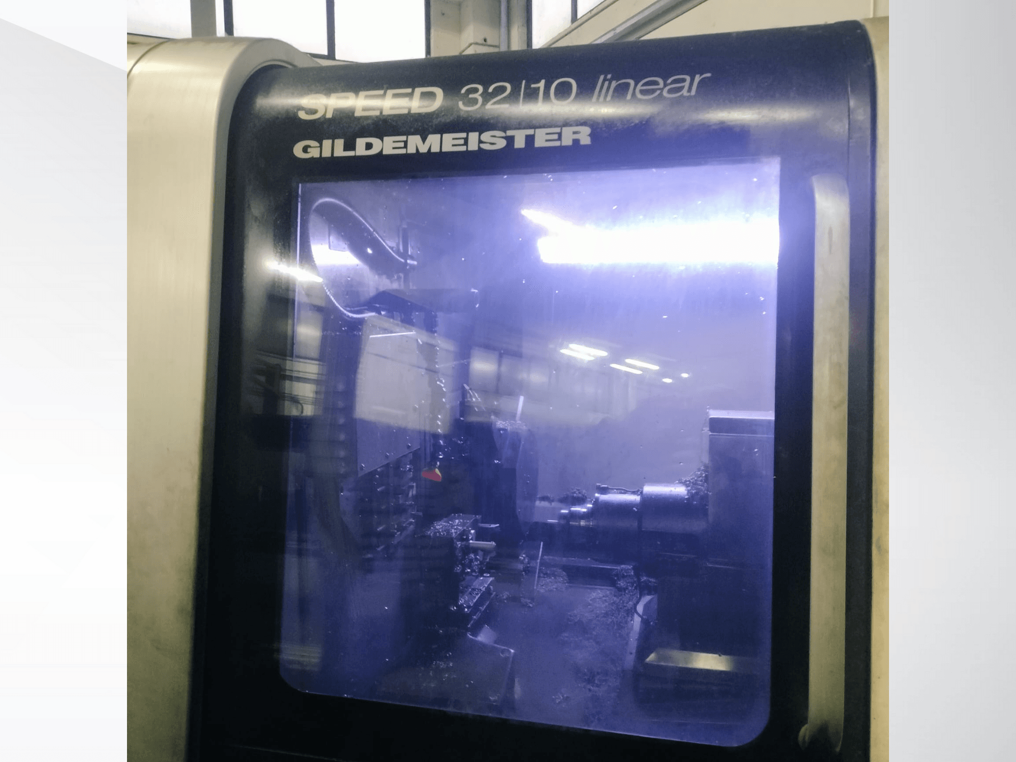 Gildemeister SPEED 3210 linjär CNC-maskin framifrån, visar interna komponenter och flytande kylmedel i drift.