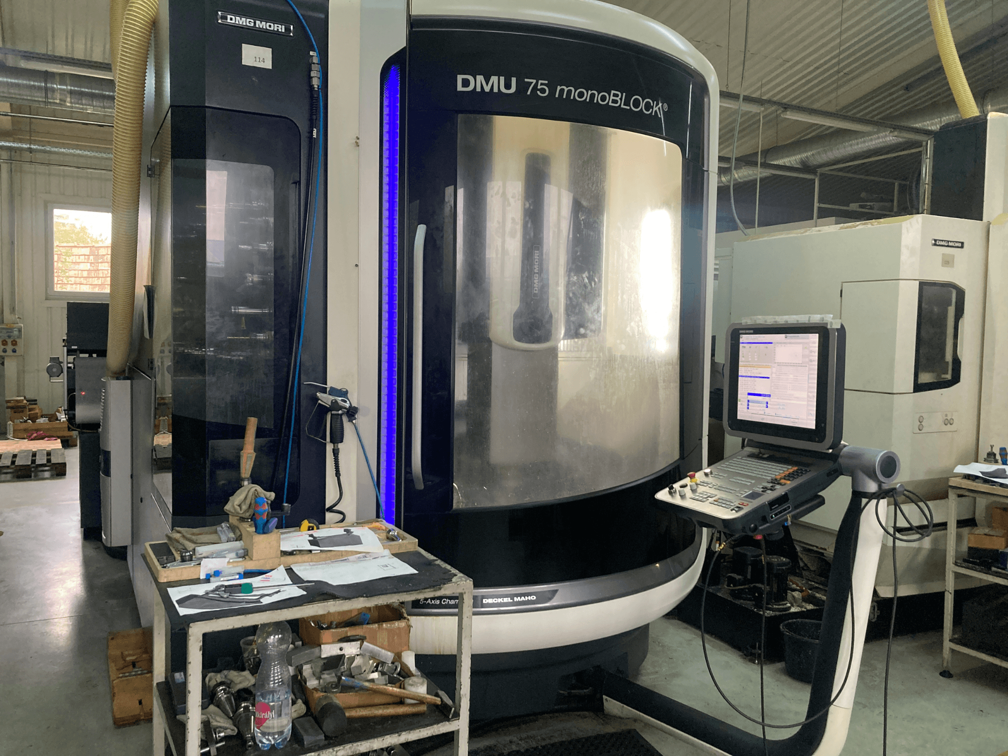 DMG MORI DMU 75 monoBLOCK® CNC-maskin, framifrån, med kontrollpanel, verktyg och en arbetsyta med material.