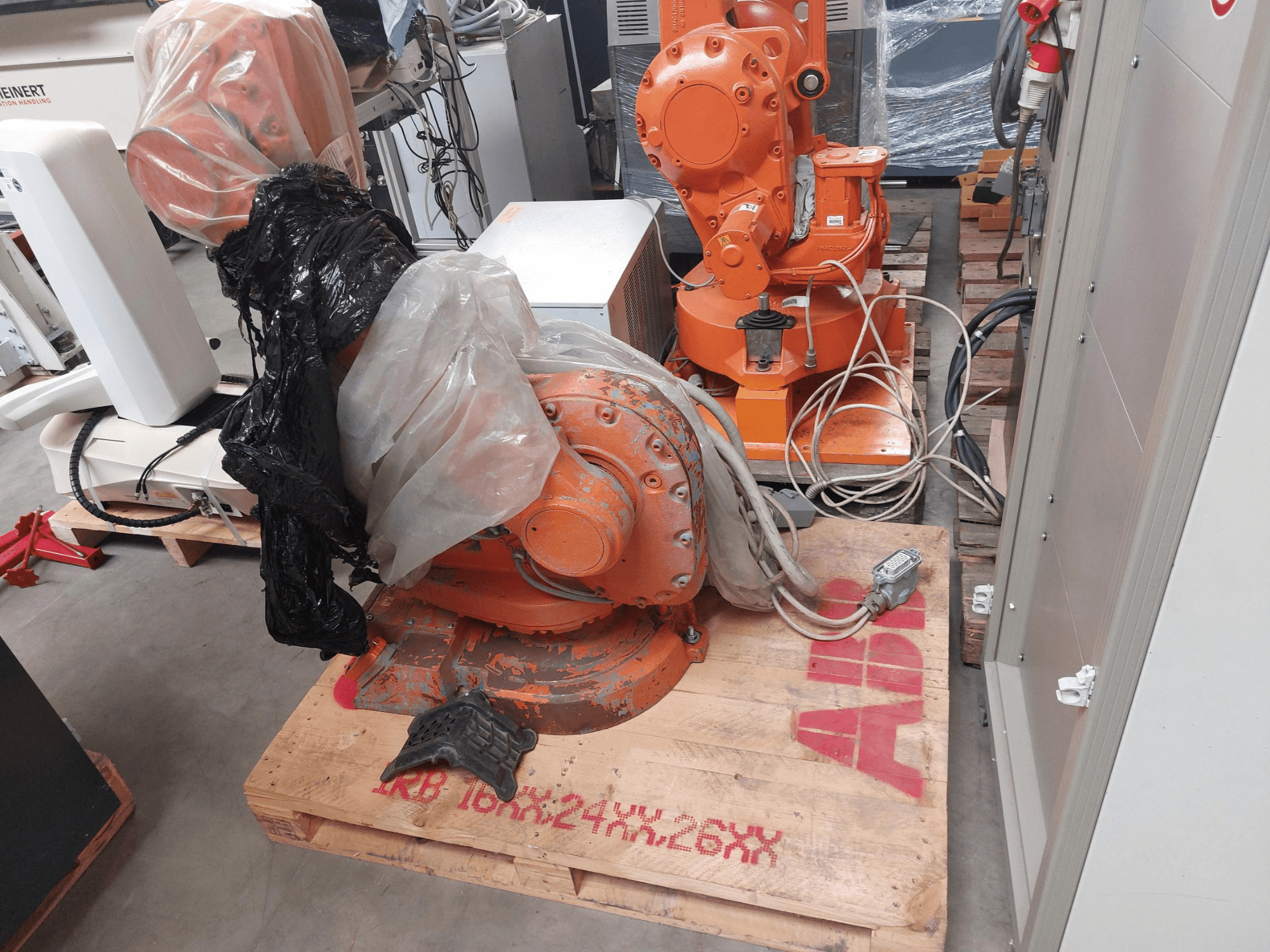 ABB IRB 1600 M2004 robotarm delvis täckt av plast, sedd framifrån, med kablar och ytterligare maskiner i närheten.