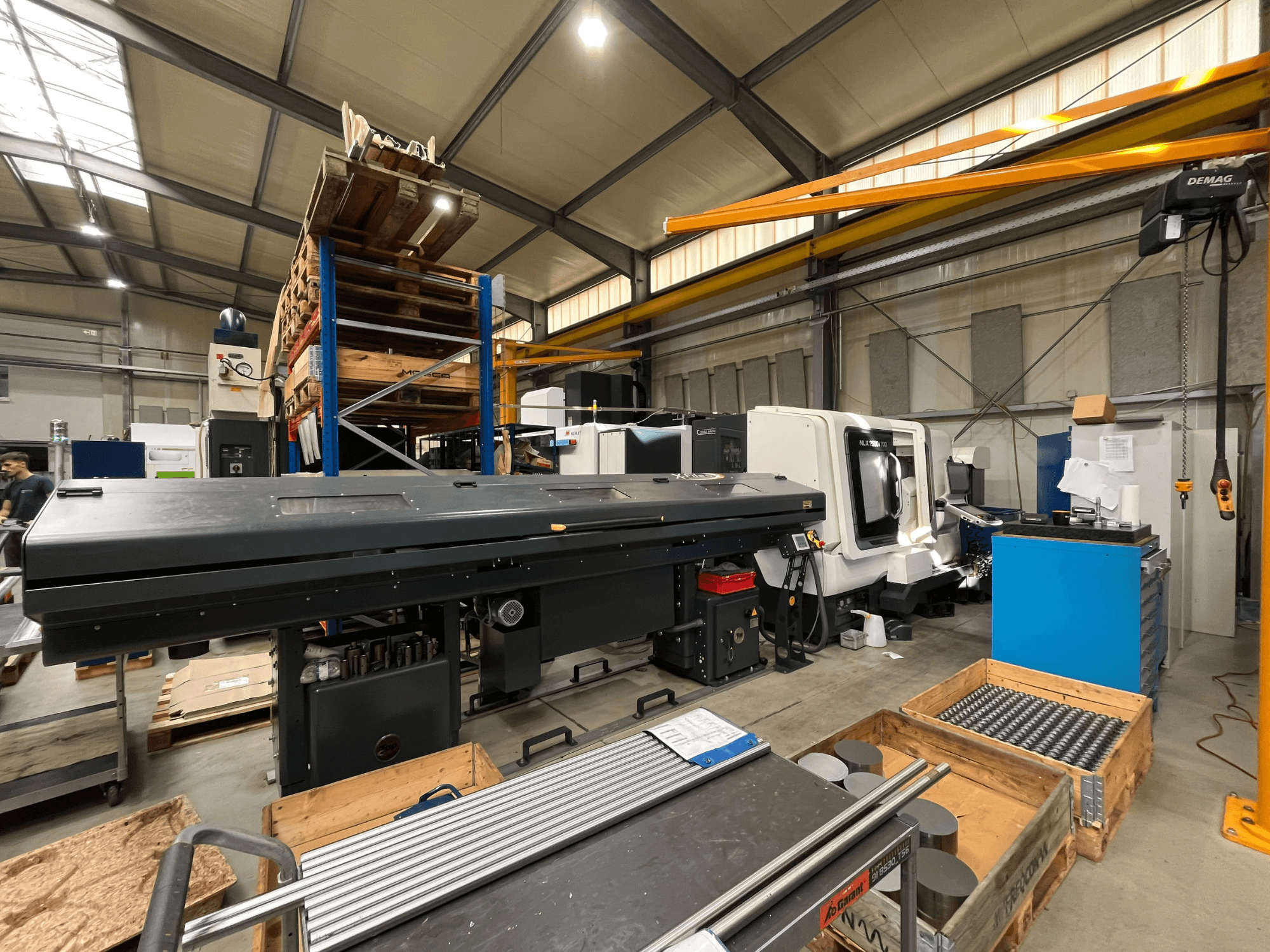 En horisontell svarv av typen DMG MORI MORI NLX 2500/700 SY i en verkstad, sedd från sidan med lagerutrymme och verktyg i bakgrunden.