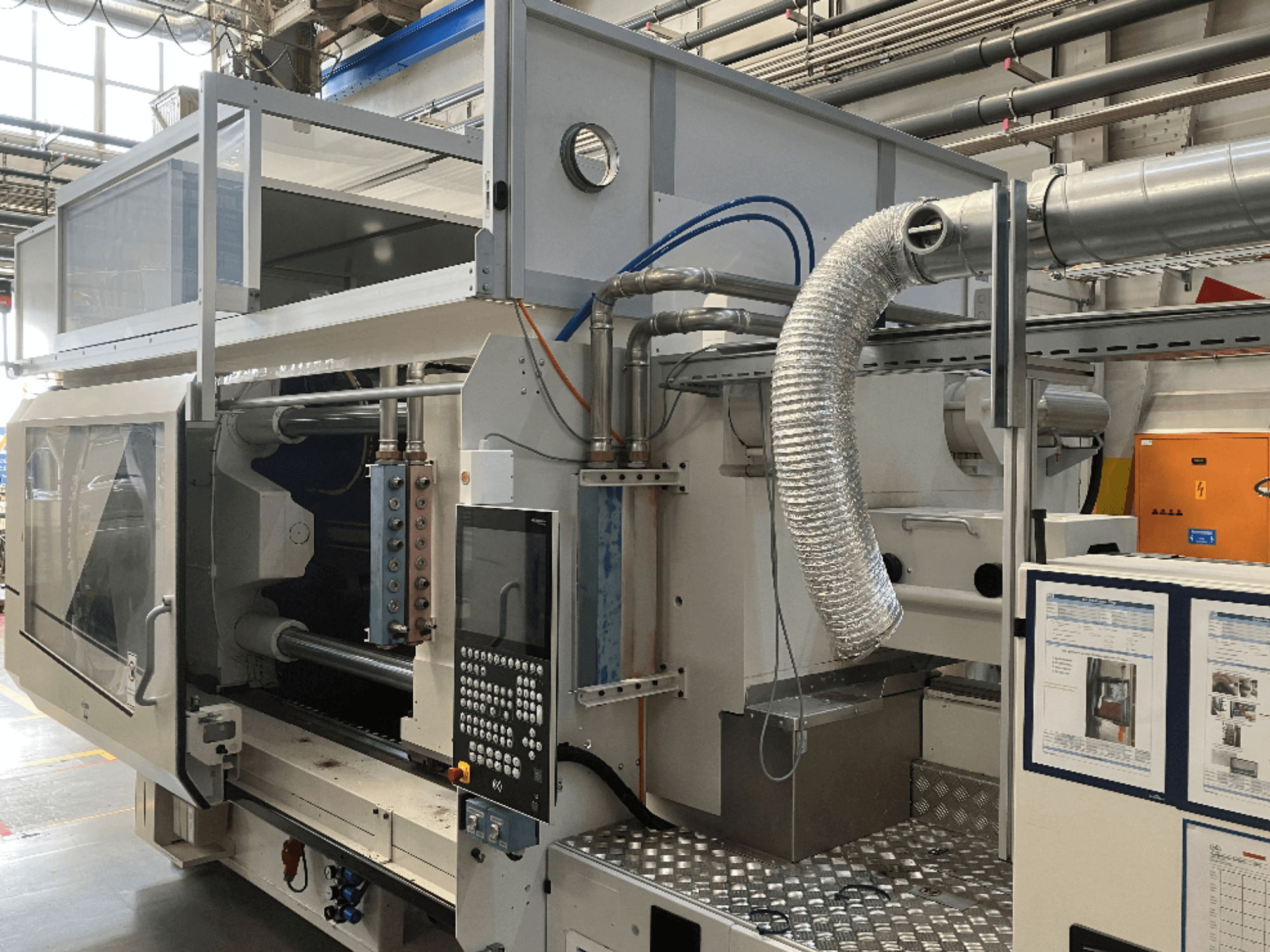 Industrimaskin från märke X, sidovy som visar kontrollpanel, kanalsystem och maskinkomponenter i en fabriksmiljö.