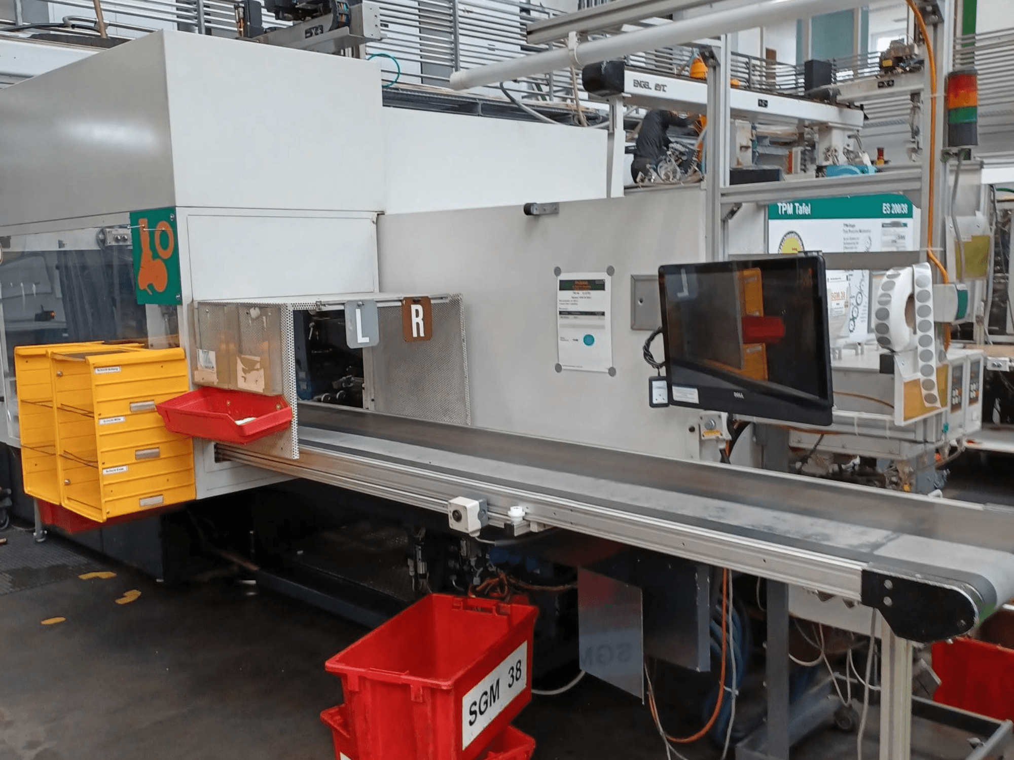 Industriell sorteringsmaskin med gula och röda fack, vy från sidan, med en kontrollmonitor och märkta fack för sortering.