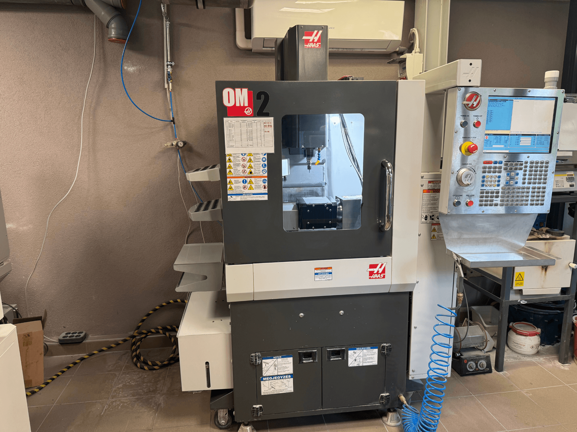 Haas CNC-maskin OM-2, framifrån, med kontrollpanel, spindel och säkerhetsetiketter, placerad i en verkstadsmiljö.
