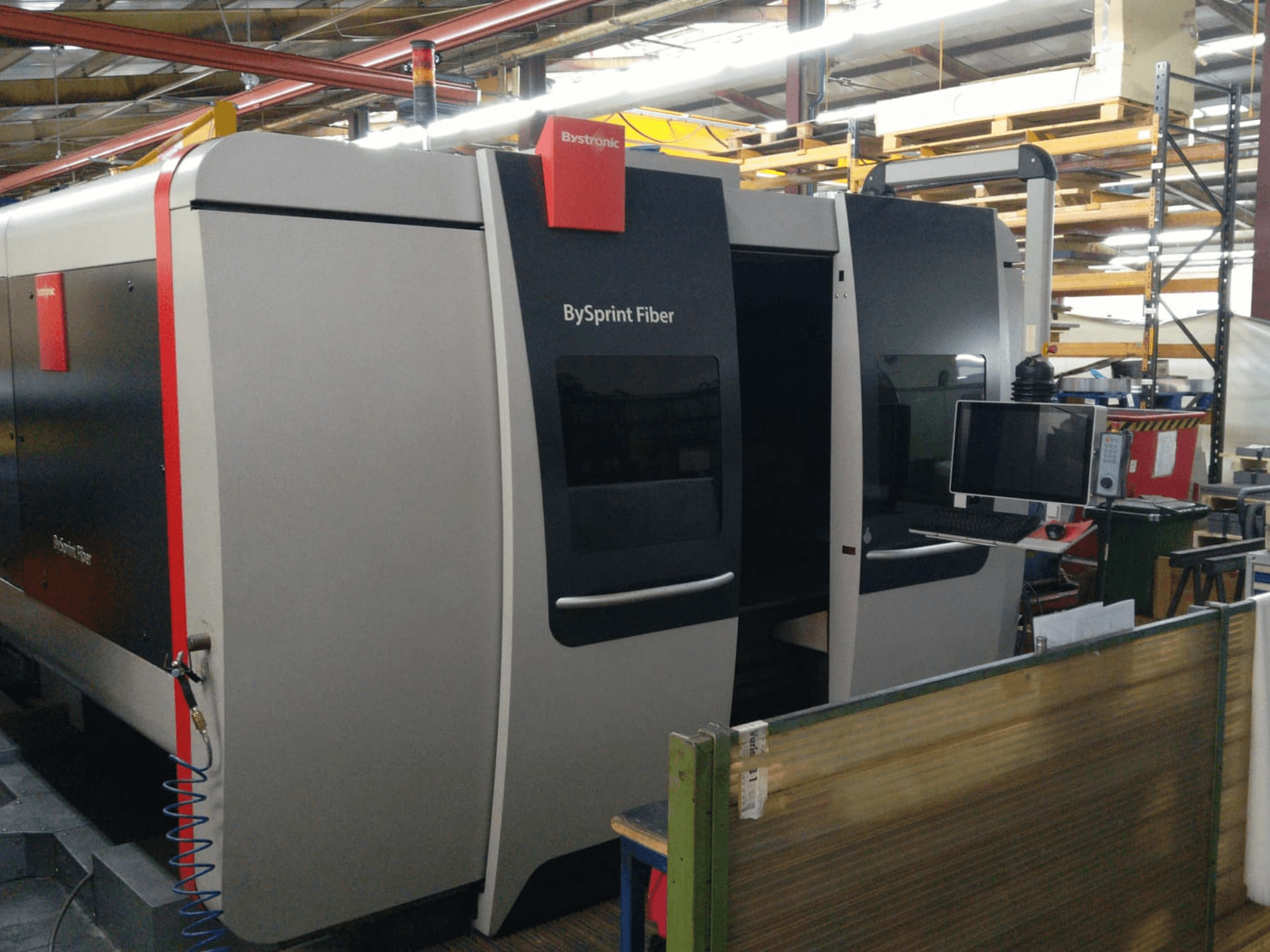 Bystronic BySprint Fiberlaserskärare, framifrån med kontrollpanel, synliga detaljer inkluderar två dörrar och en monitor på sidan.