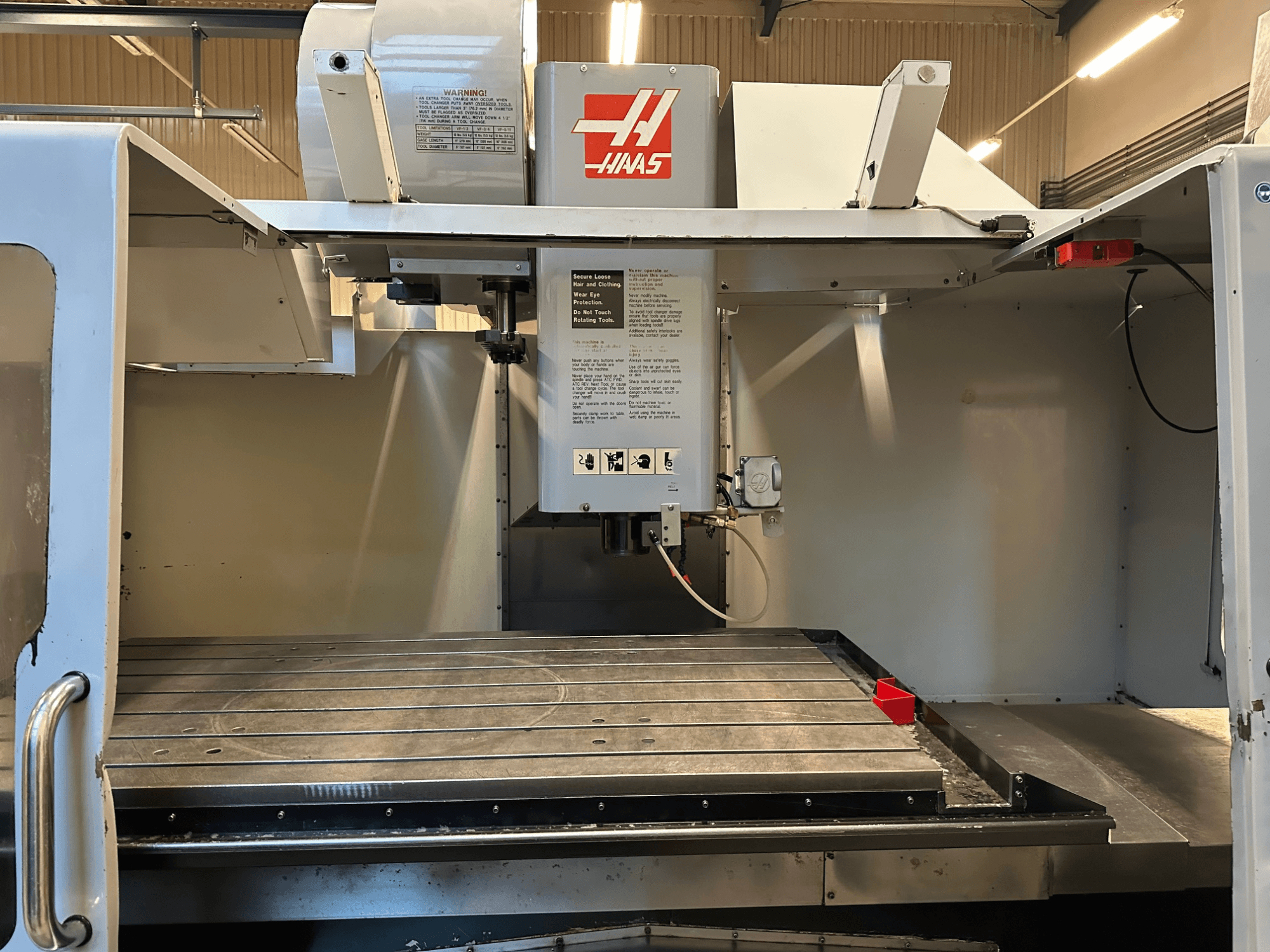 Haas CNC-fräsmaskin, modell VF-2, framifrån med reglage, arbetsbord i metall och säkerhetsetikett på panelen.