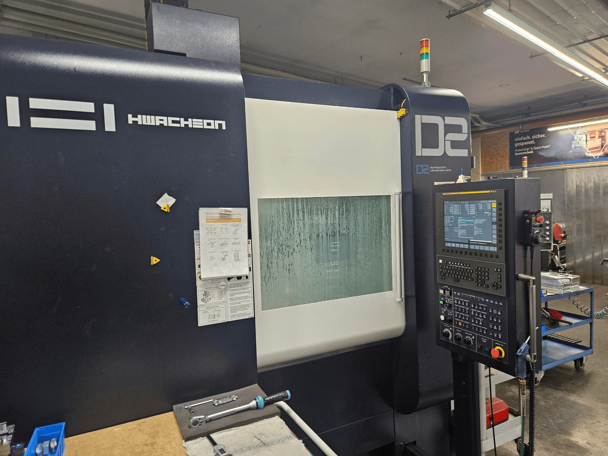 HWACHEON D2-5AX 12k vertikalt bearbetningscenter, framifrån med kontrollpanelen och det immiga fönstret.