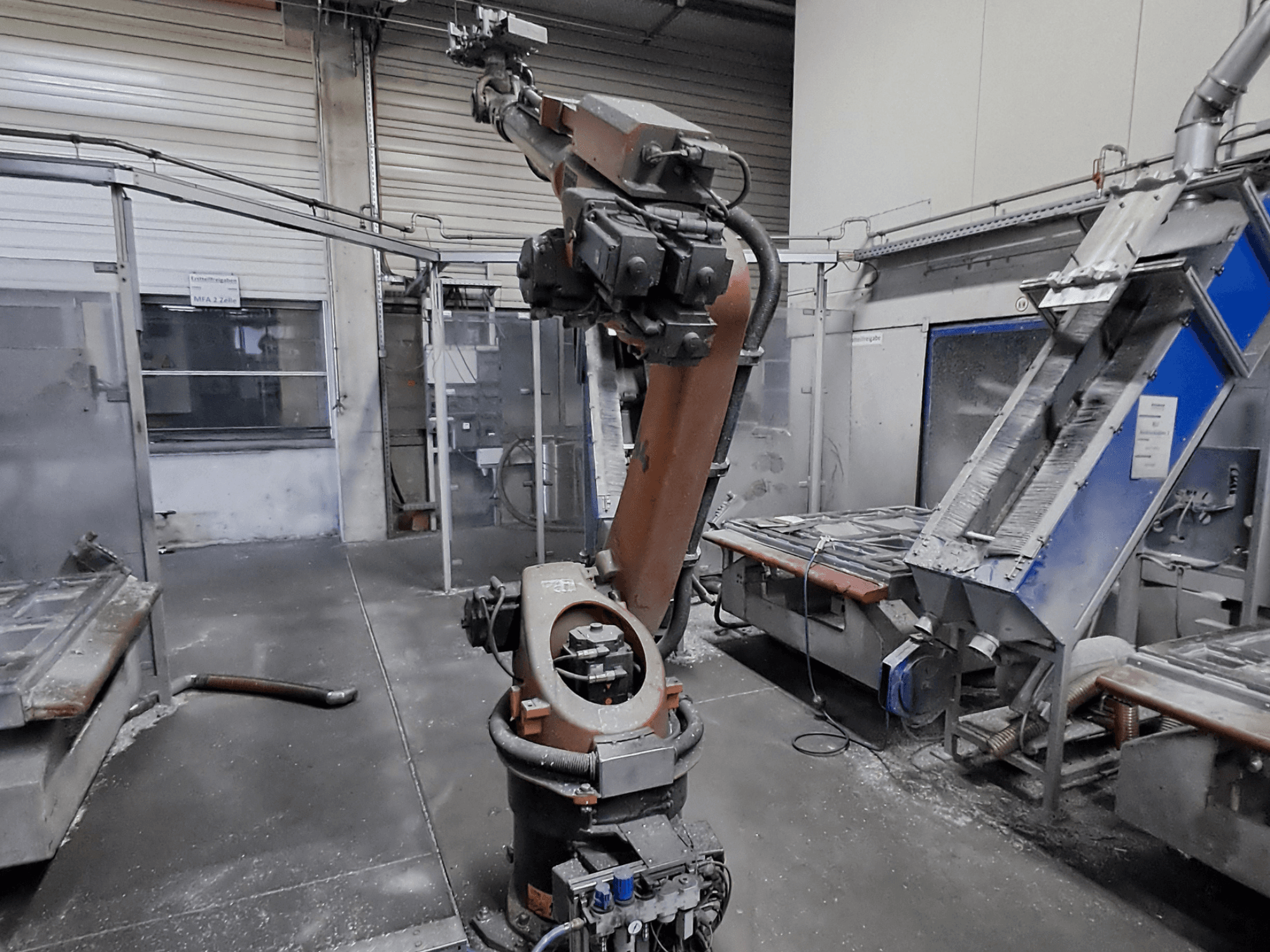 En KUKA KR 30L16-2-robotarm i en verkstadsmiljö, sett framifrån, med synligt damm och maskiner i bakgrunden.