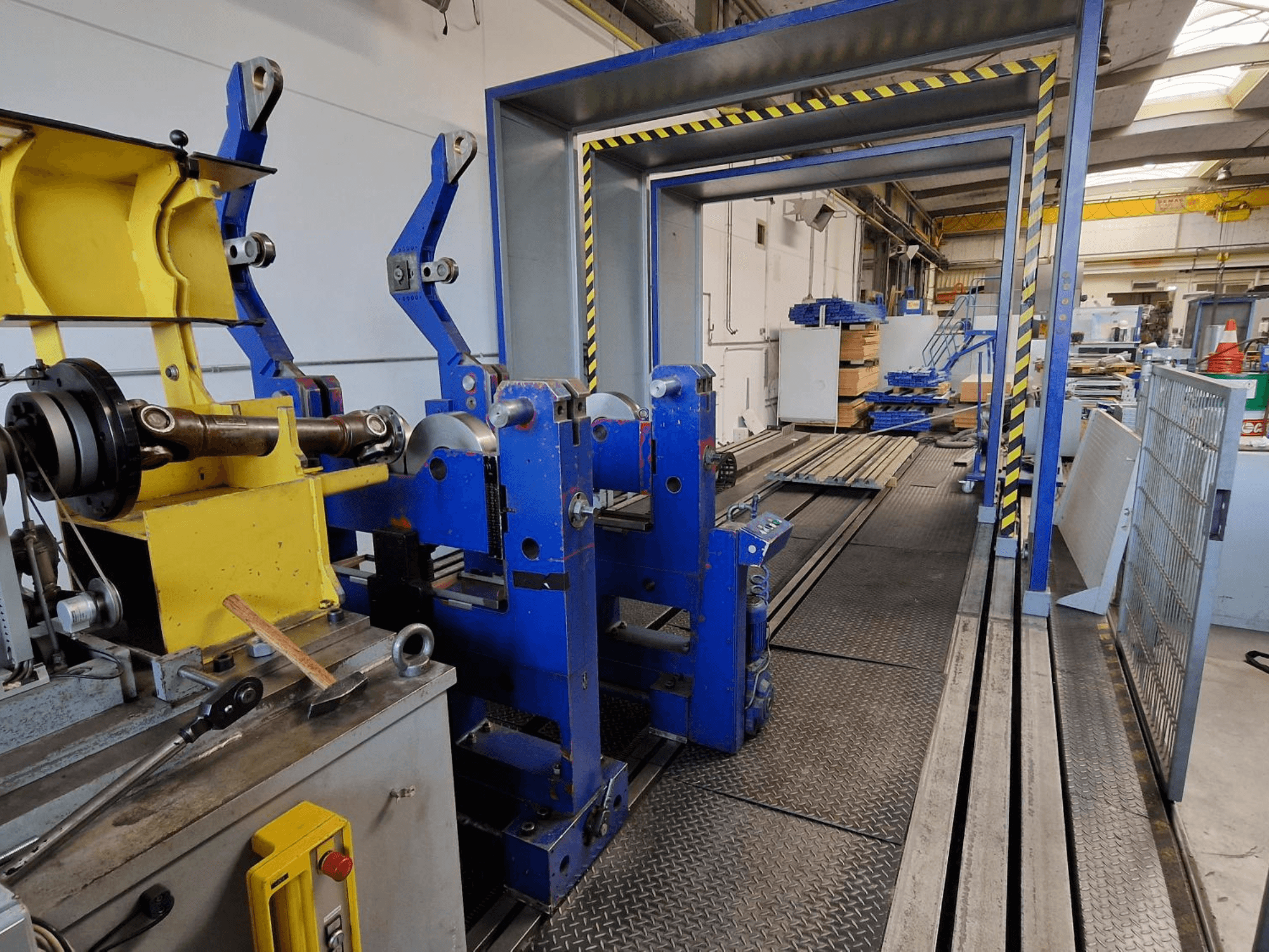 Verktygsmaskin SCHENCK HM 70U BU, sidovy som visar den blå konstruktionen med gula komponenter och kontrollpanelen i en industriell miljö.